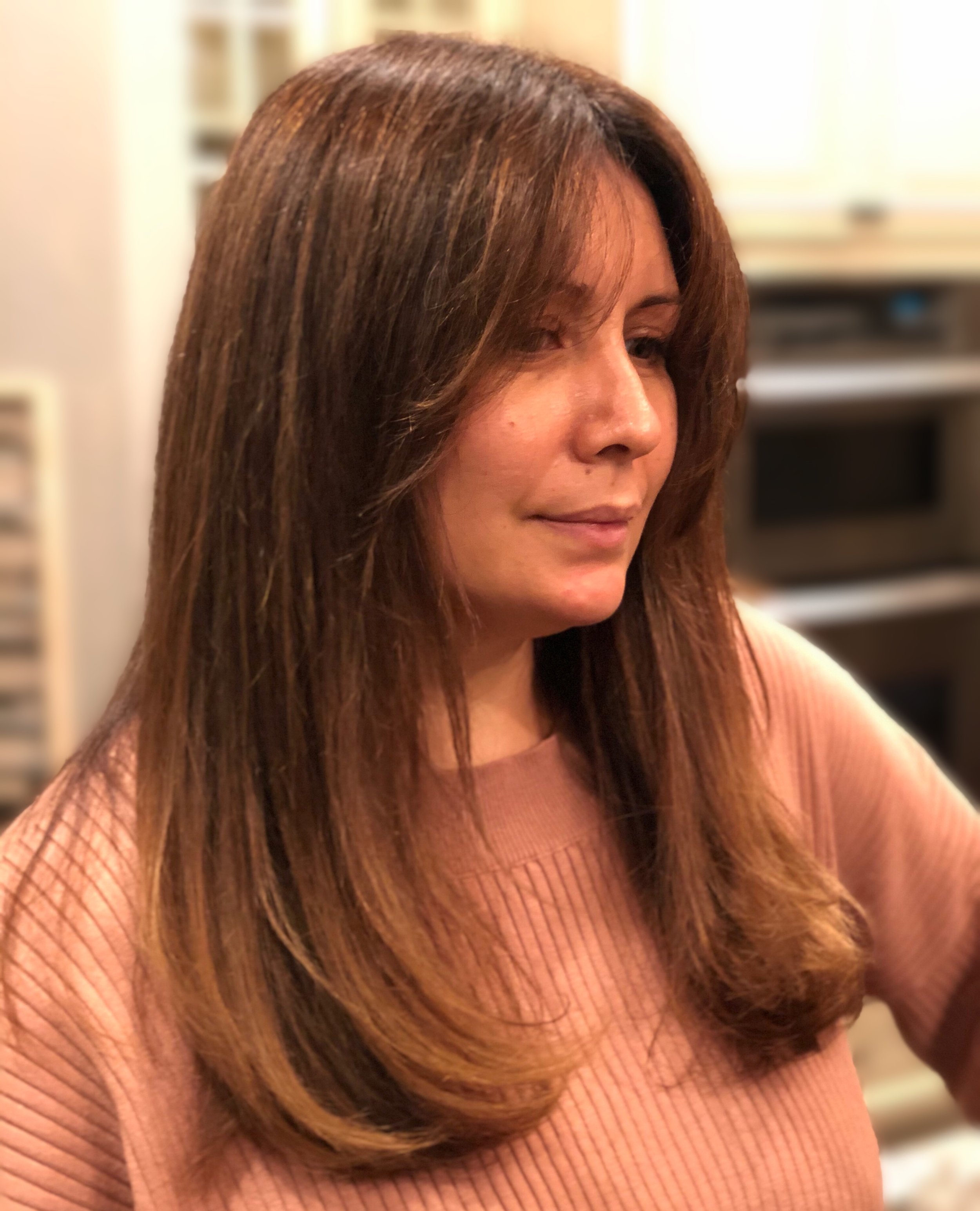 Woman with long brown hair wearing a pink sweater indoors.