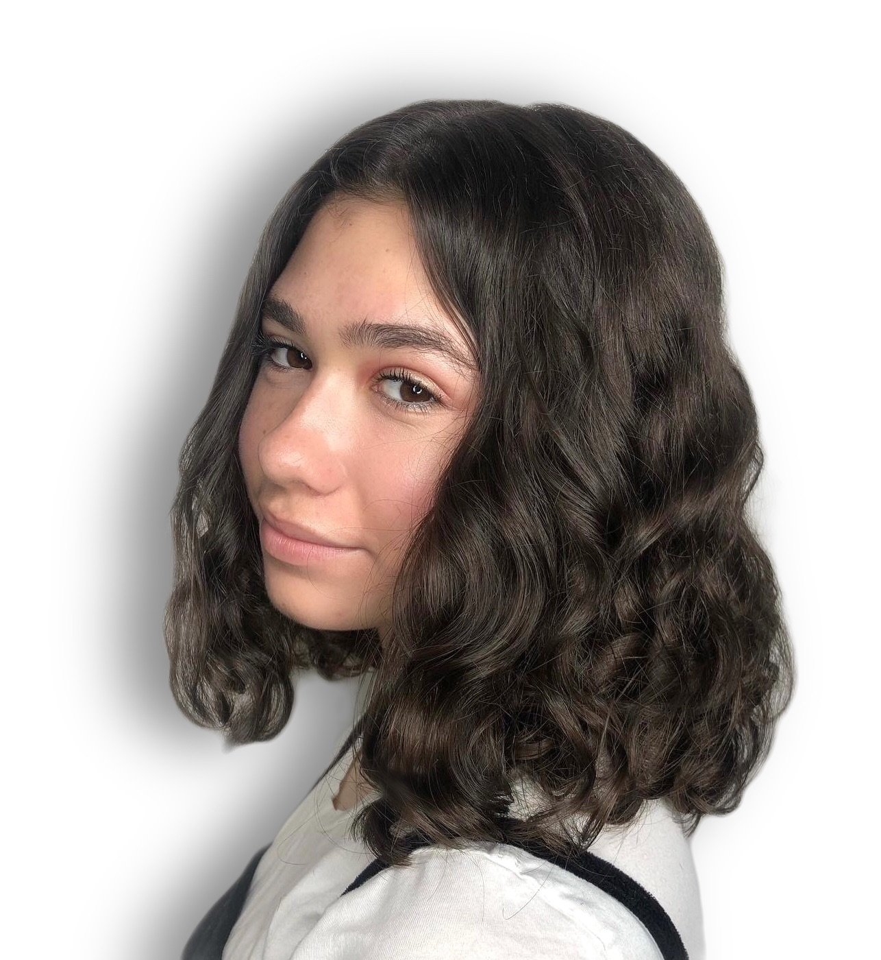 Person with curly dark hair, wearing a white top with black straps, looking at the camera on a white background.