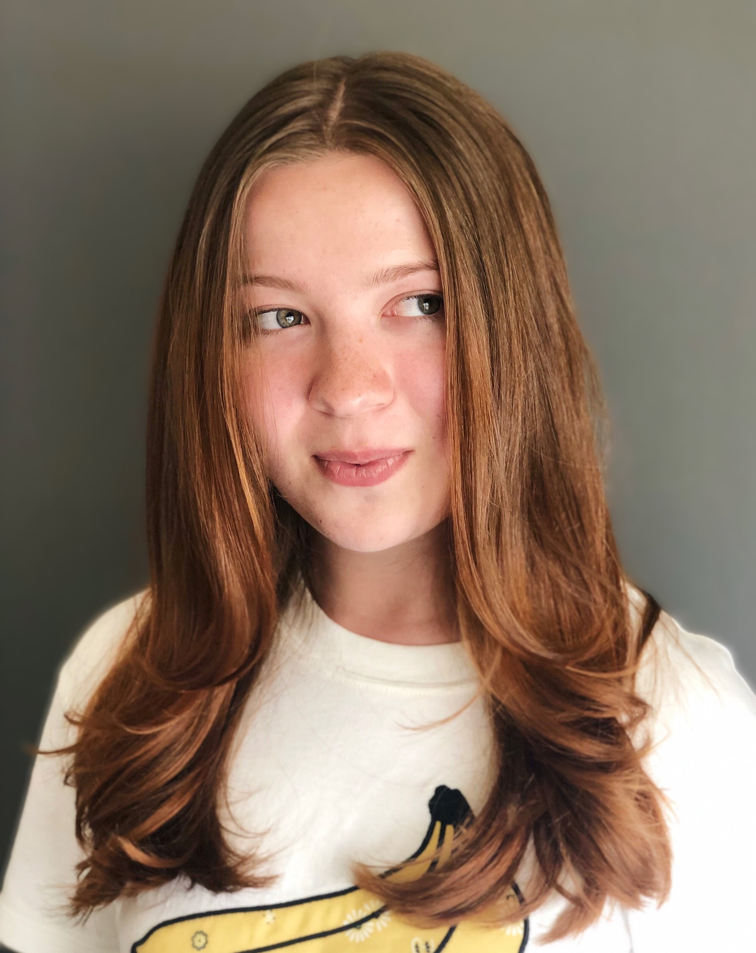 Portrait of a young person with long, light brown hair, looking to the side, wearing a white shirt with a banana graphic.