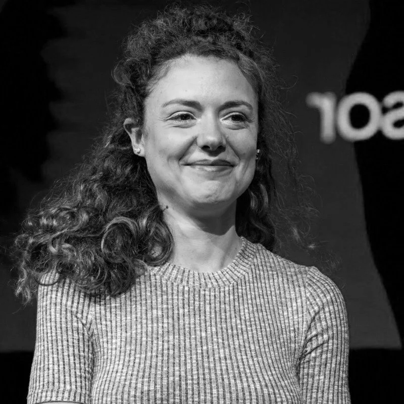 Black and white photo of a woman with curly hair, smiling gently, wearing a striped shirt.