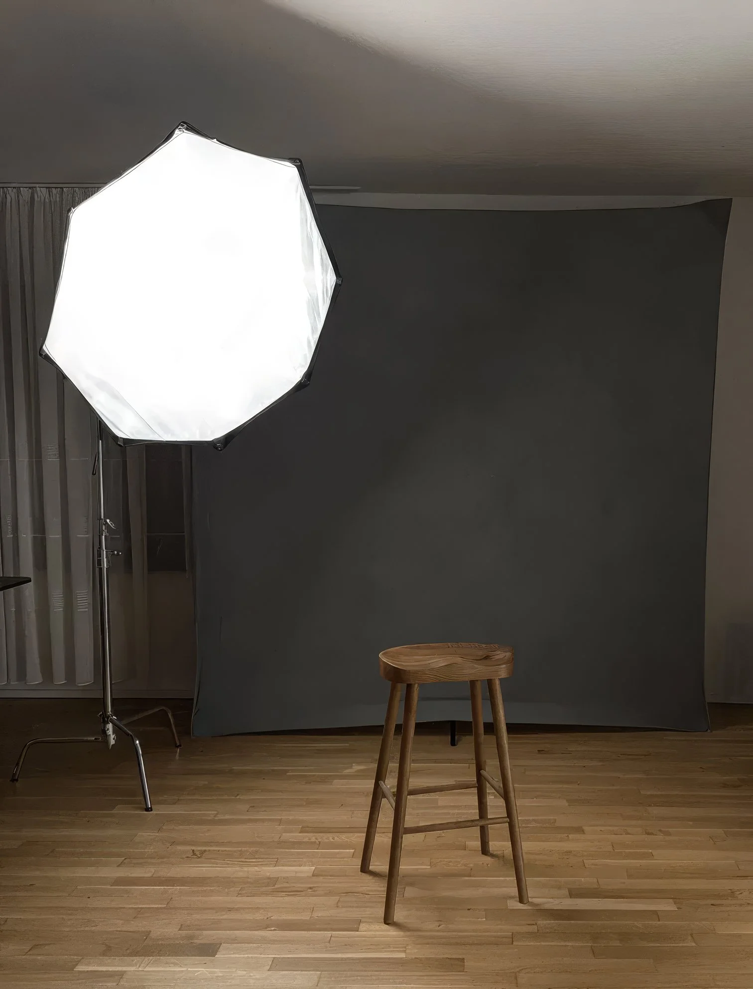 Empty wooden stool under a glowing octobox softbox against a grey backdrop in a Frankfurt home photography studio, set up for a private men's portrait session.