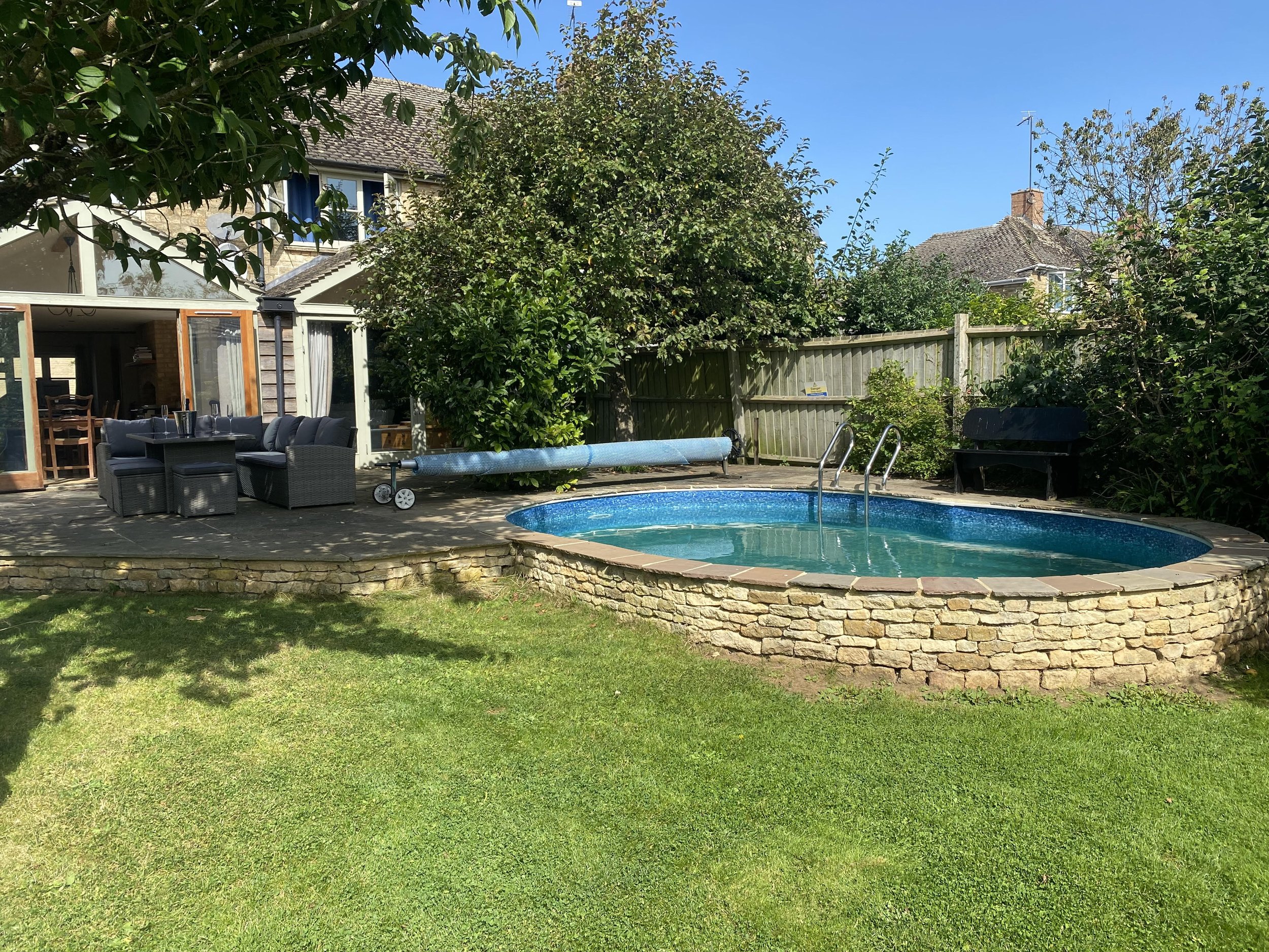 Private swimming pool and garden leading off patio area that adjoins open plan dining area from main house in Cotswolds area of UK.