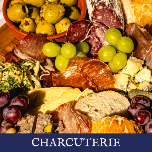 A charcuterie board with various cheeses, grapes, cured meats, green olives, and bread.