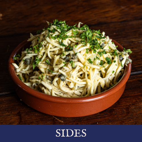 A bowl of pasta with herbs and capers on a wooden table.