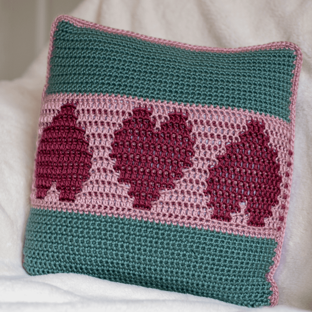 simply love mosaic crocheted cushion cover in pink and green sitting on a cream blanket tiny.png