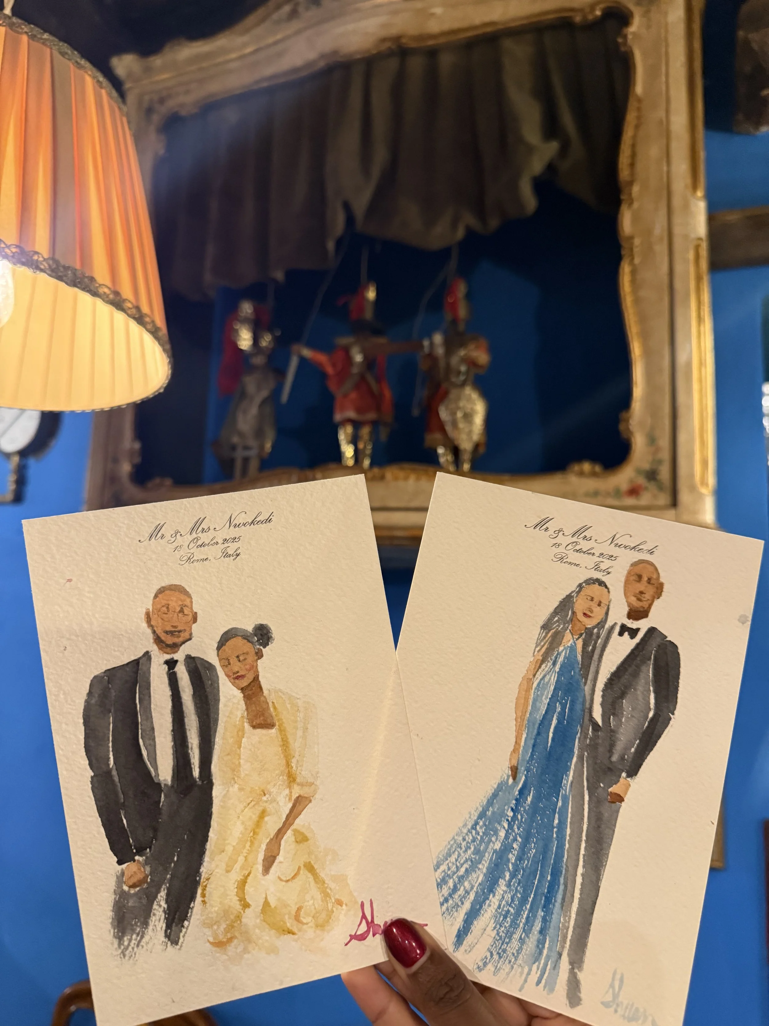 Two Italy wedding entertainment favors being held up, each featuring a couple in formal attire, with a blue background and antique figurines in a glass case behind them.