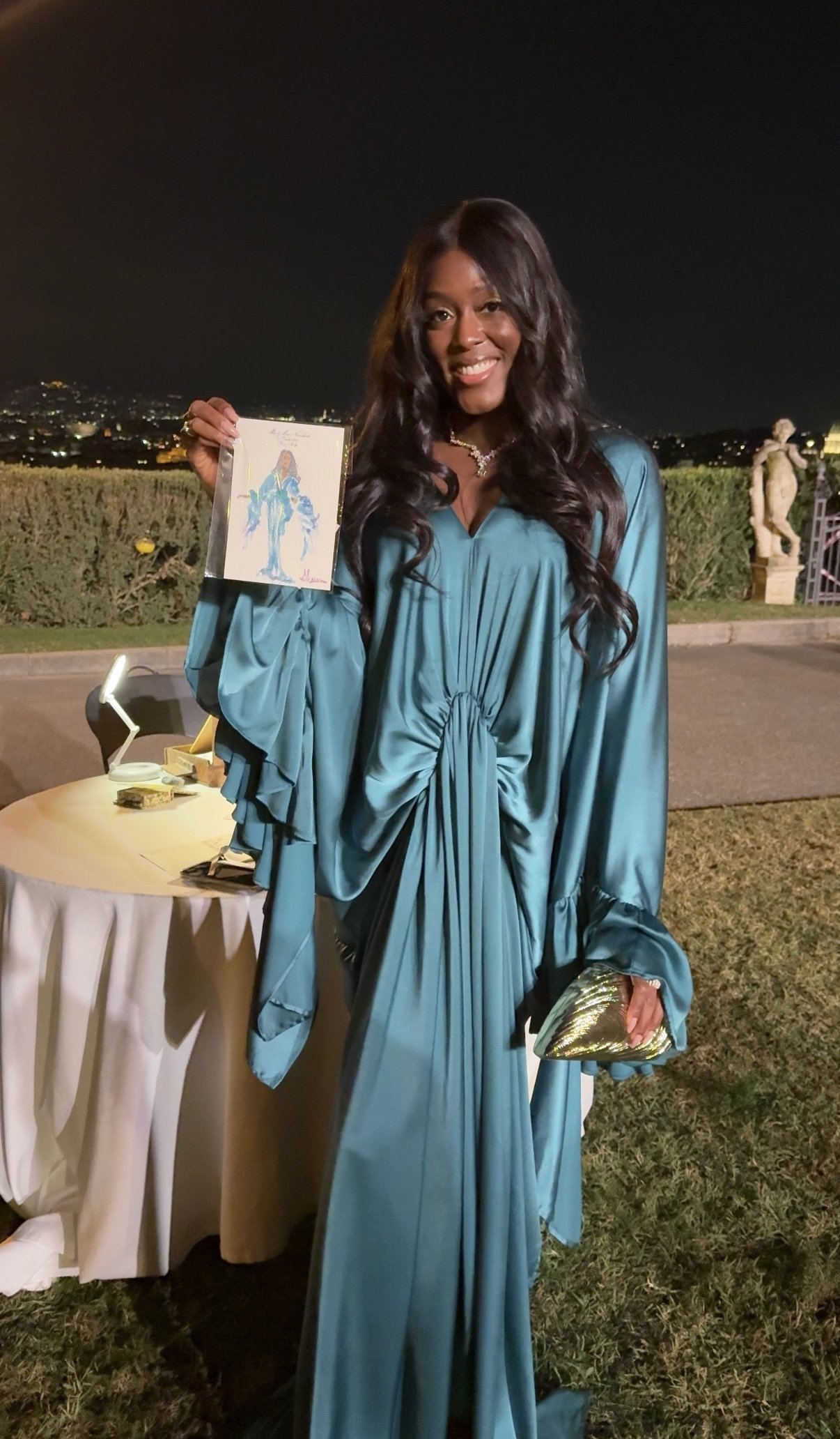 A woman wearing a teal satin gown holds an elegant watercolor guest illustration as personalized Italy wedding favor: