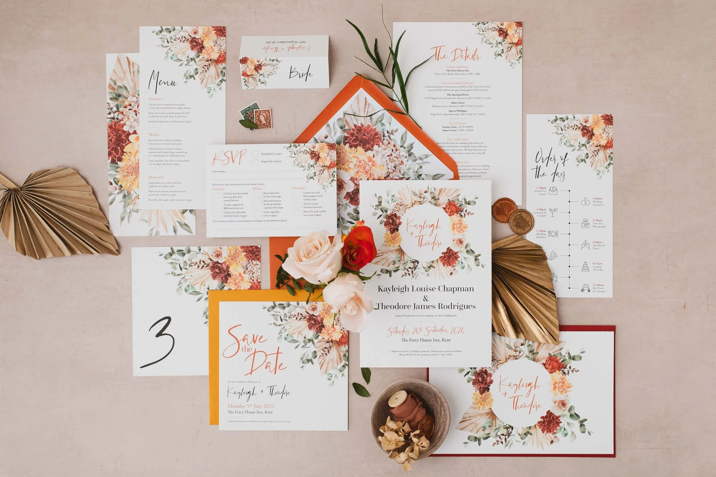 Autumnal wedding invitations with burnt orange floral design, RSVP card, menu, schedule, and save-the-date card arranged on a light pink surface with decorative dried leaves, flowers, and wax seals.