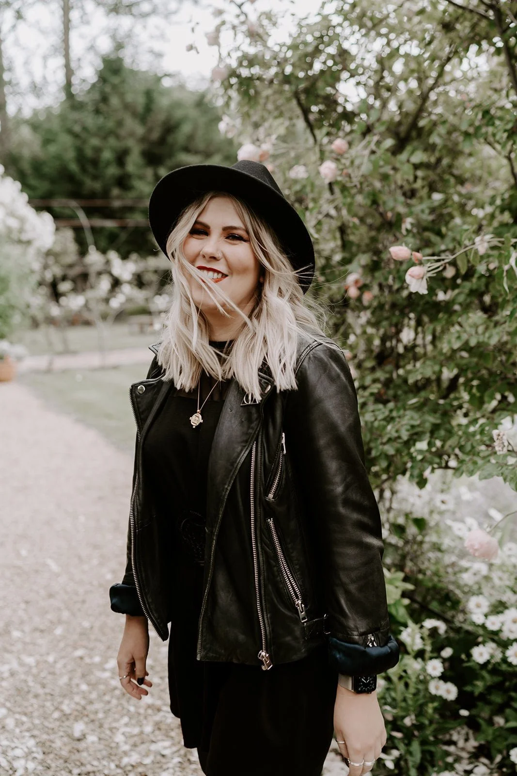 Emily, owner of Wild Moon Wedding Stationery in a garden in Stamford wearing a black hat and leather jacket.