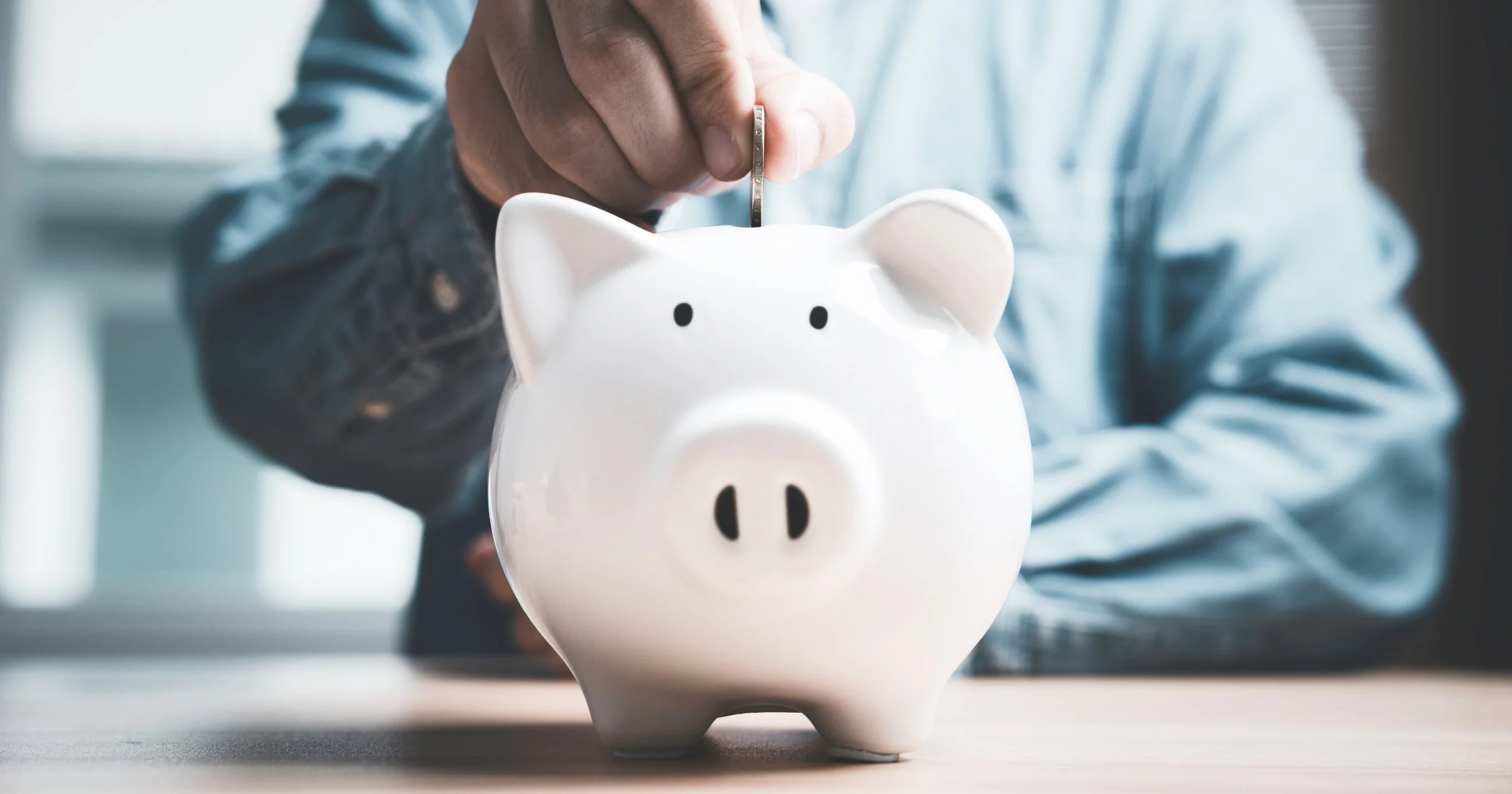 Person putting coin into white piggy bank