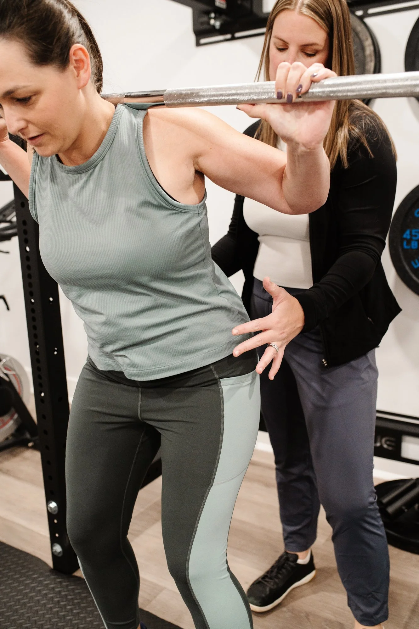 A pelvic floor physical therapist using functional pelvic floor exercises on a patient using a barbell in pelvic floor PT.