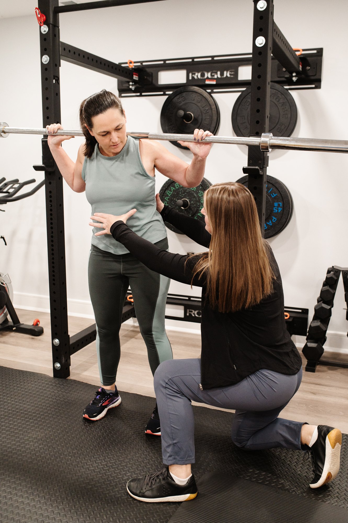 A pelvic floor physical therapist doing functional exercises with a patient during a pelvic floor PT session using a squat bar.