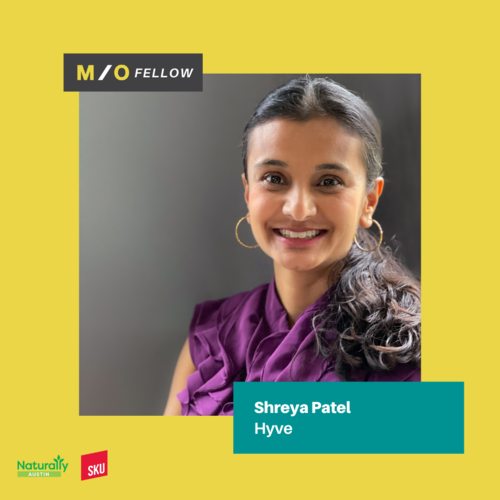Smiling woman with dark hair and hoop earrings, wearing a purple top, portrait with a yellow background, indicating she is a MO Fellow named Shreya Patel from Hyve.