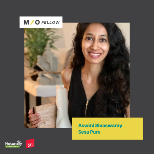 A woman with long curly black hair, smiling and holding a book or notebook in her hand, standing indoors with a plant and a bookshelf in the background. The image includes text indicating she is an M/O Fellow named Aswini Sivaswamy Sesa Pure and has 