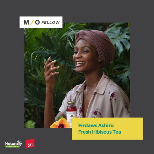 A woman with a pink headwrap smiling and holding a glass jar of Firdaws Ashiru Fresh Hibiscus Tea in front of lush green plants.