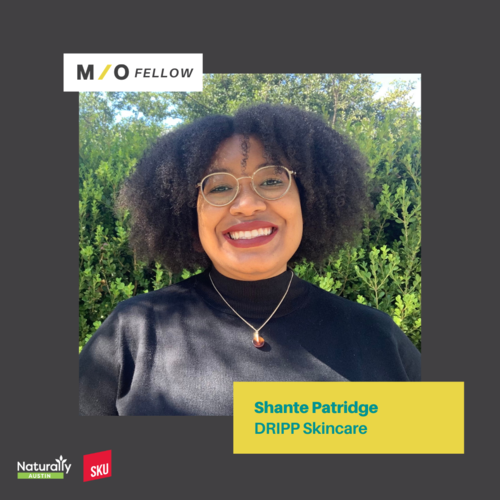 Close-up of a smiling woman with glasses and curly hair outdoors, with text indicating she is Shante Patridge from DRIPP Skincare, part of M/O Fellow program.