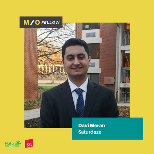 Portrait of Davi Meran in a suit smiling outside with a building and trees in the background, on a yellow promotional card for M/O Fellow.