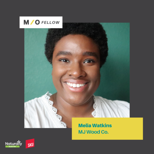 A smiling young Black woman with short, curly hair, wearing a white blouse with lace detail, in front of a green background. The image features a graphic design with text indicating she is a 'M/O Fellow' named Melia Watkins at MJ Wood Co.