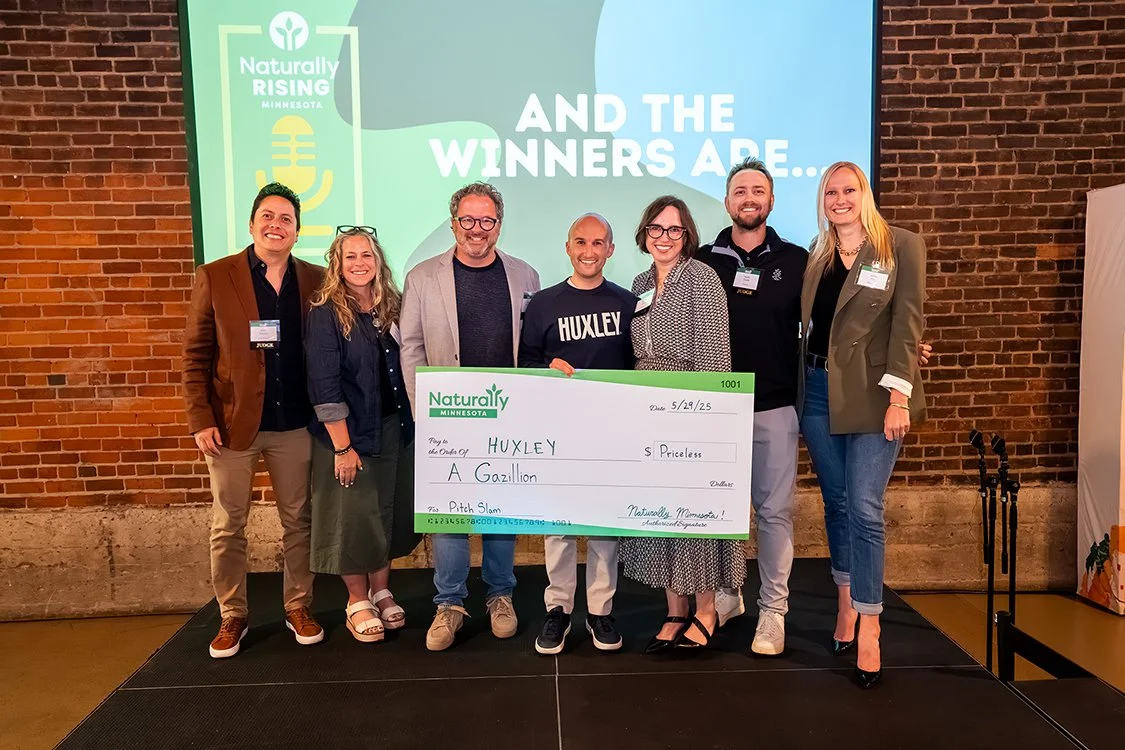 winner holding large check on stage with panel of judges
