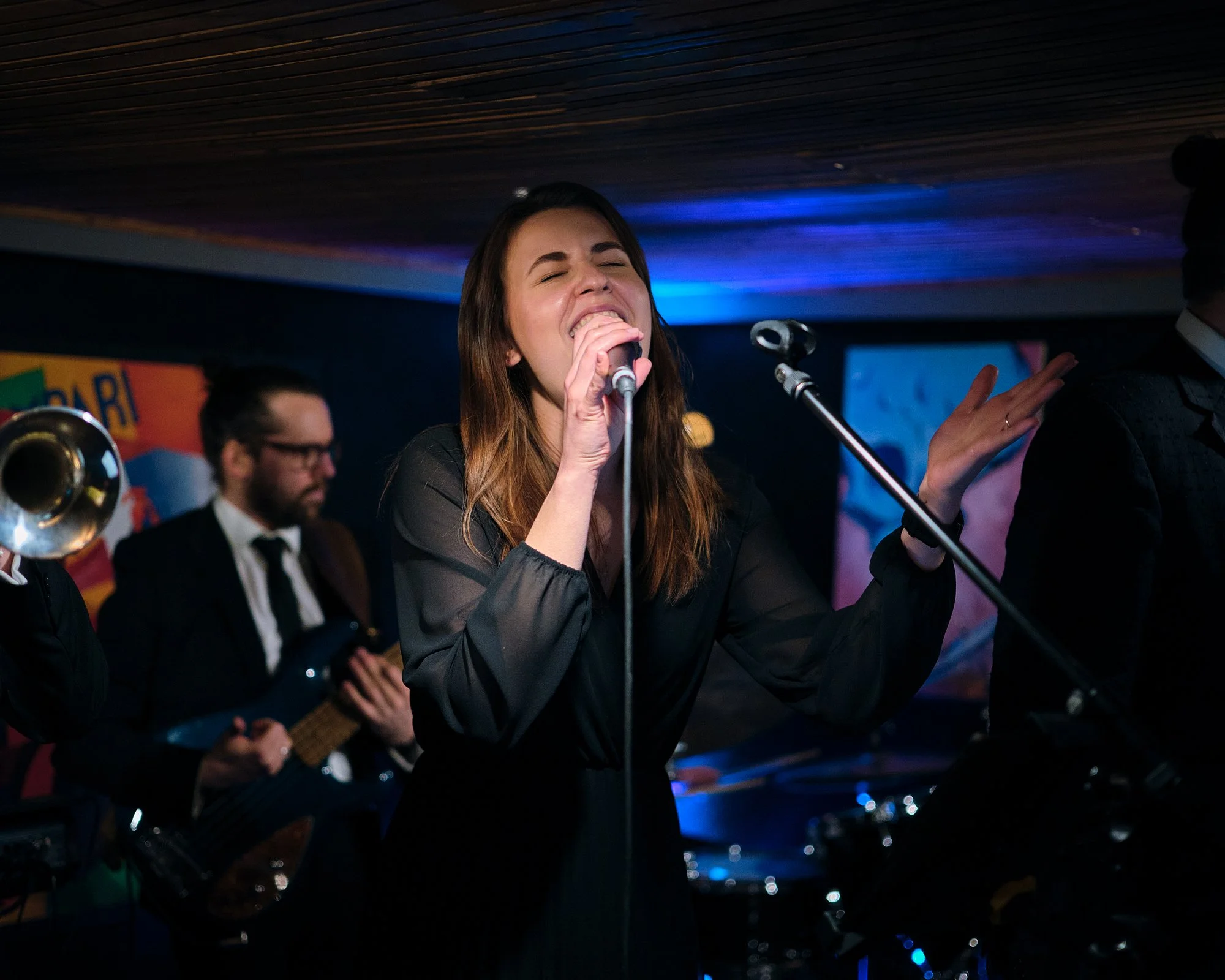A woman singing passionately into a microphone during a live band performance at a nightclub.