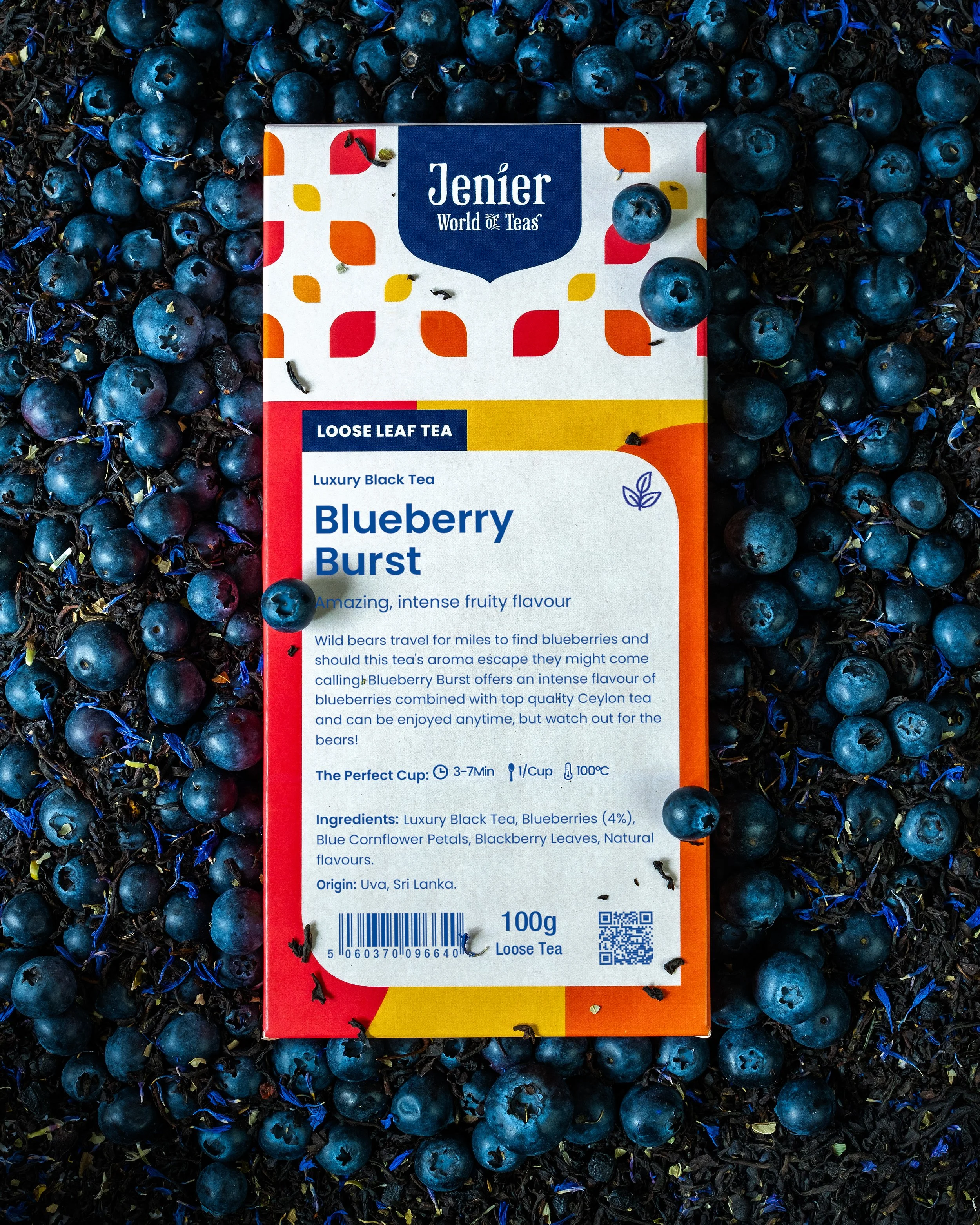 A box of Jenier Loose Leaf Blueberry Burst tea surrounded by fresh blueberries and some loose tea leaves.