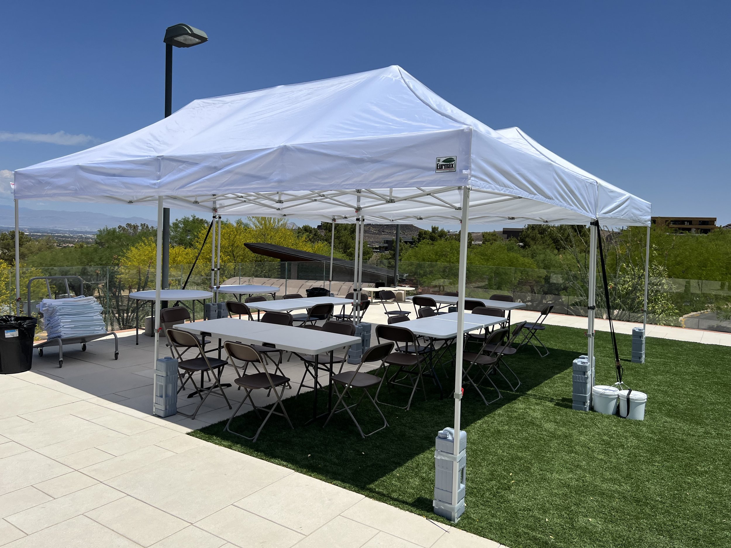Outdoor event setup with white canopy tent, folding tables, and chairs on a grassy area