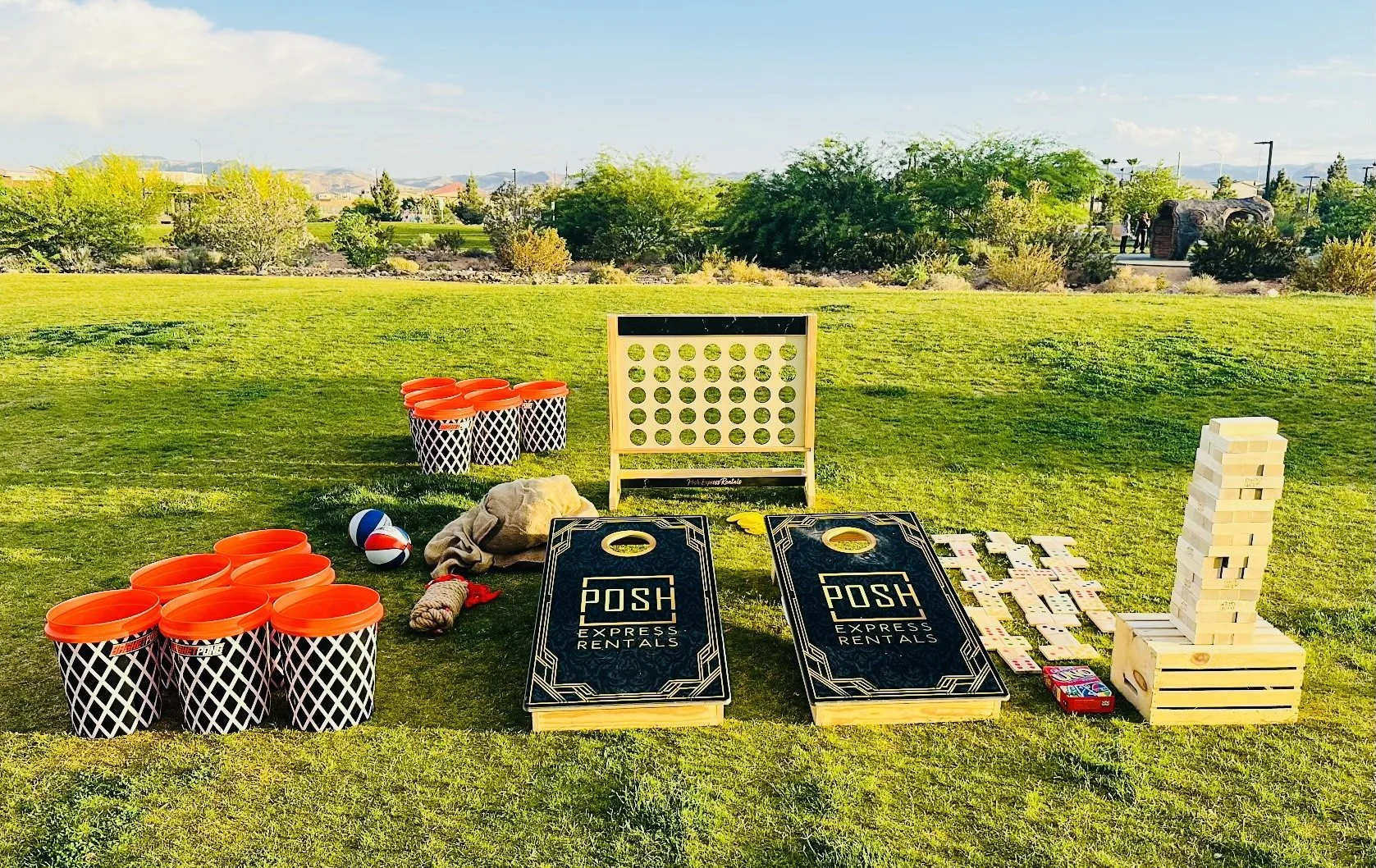 Outdoor lawn games setup on grass, including a giant Connect 4, large Jenga blocks, cornhole boards with 'POSH Express Rentals' branding, numbered buckets, and a lawn dice game set.