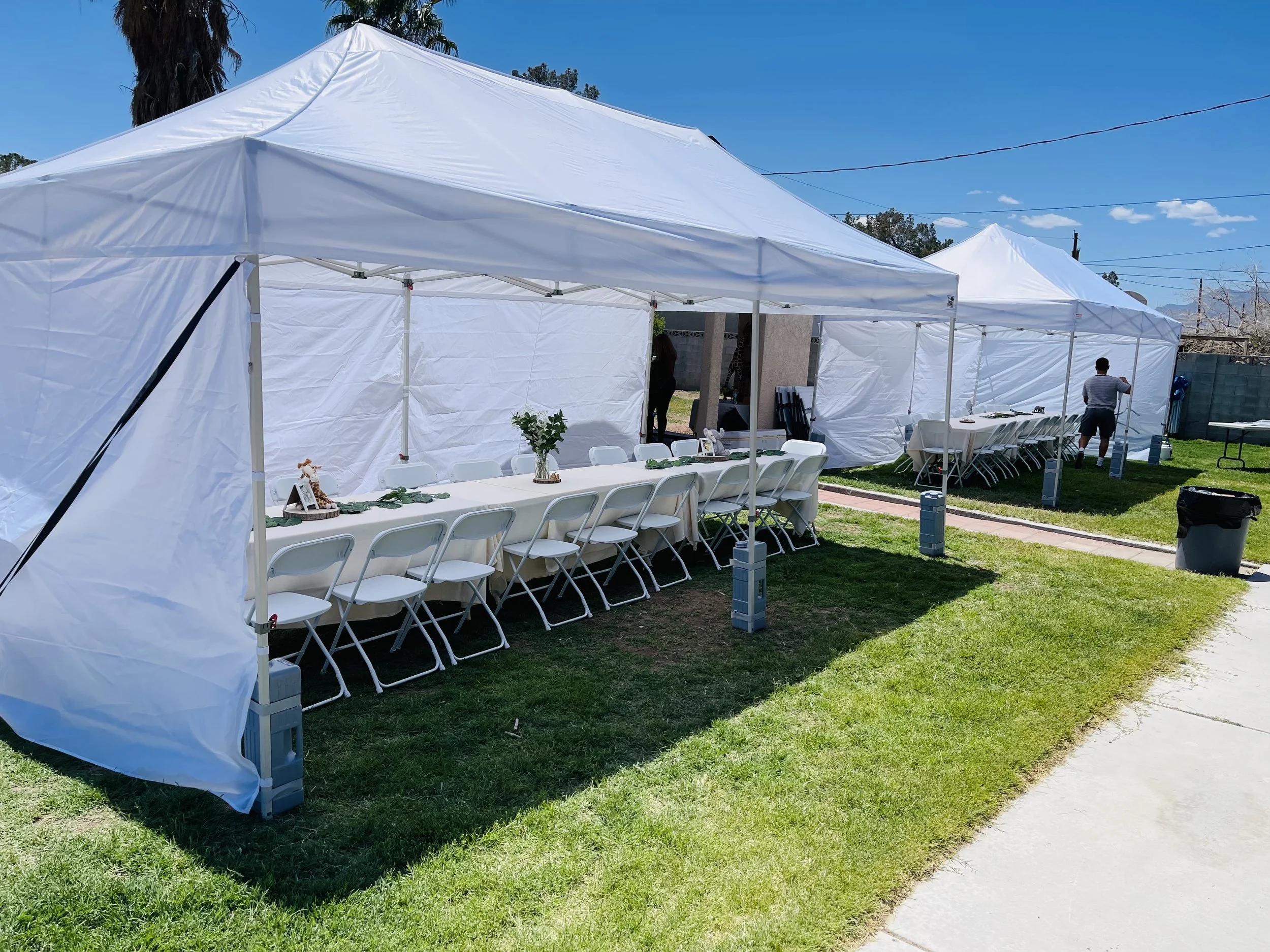 Outdoor event setup with white tents, tables, and chairs on grass