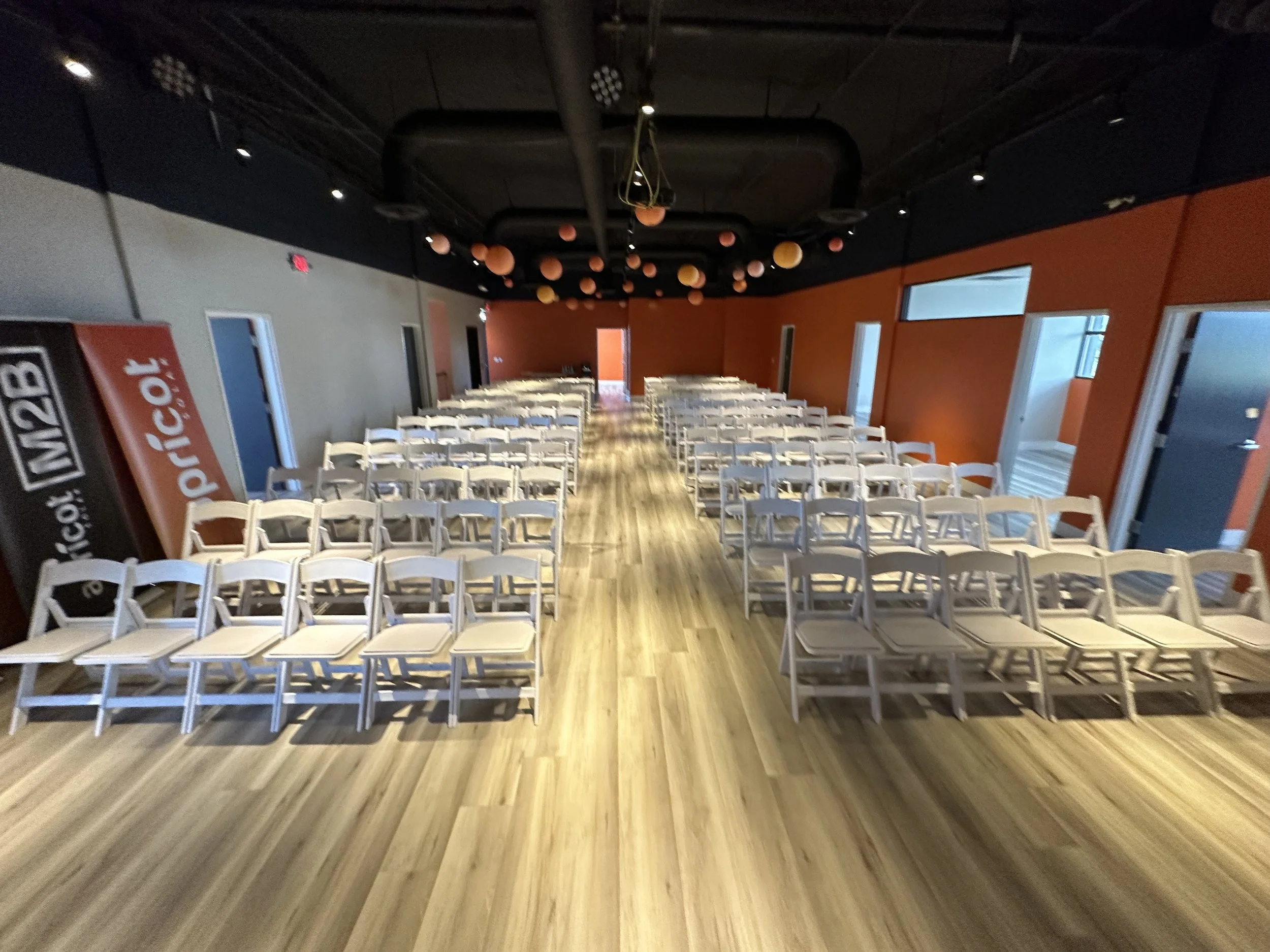 Rows of white chairs in a room with orange walls and ceiling decorations