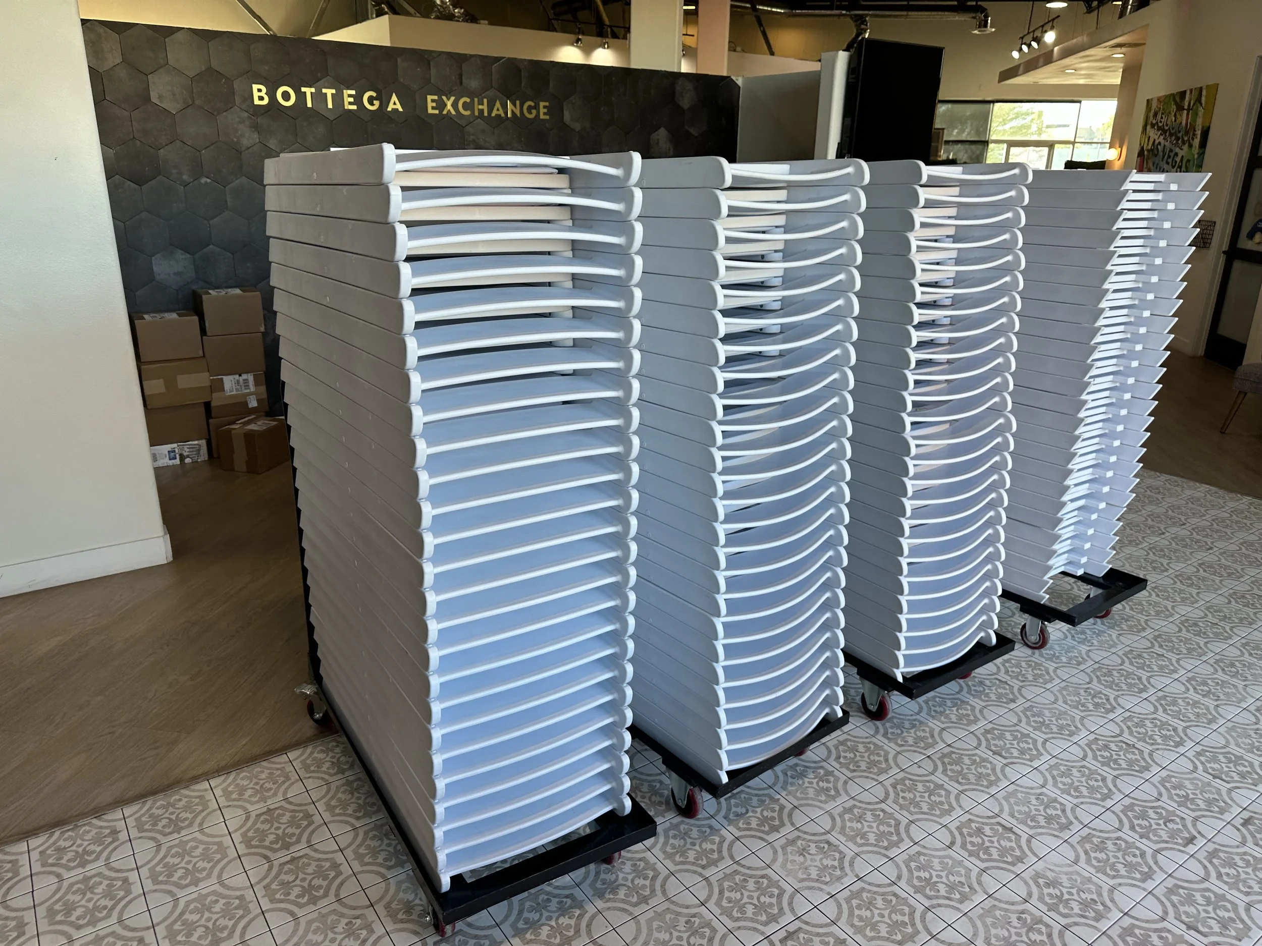 Stacks of white trays on wheeled carts inside a building with a tiled floor and a black hexagonal wall.
