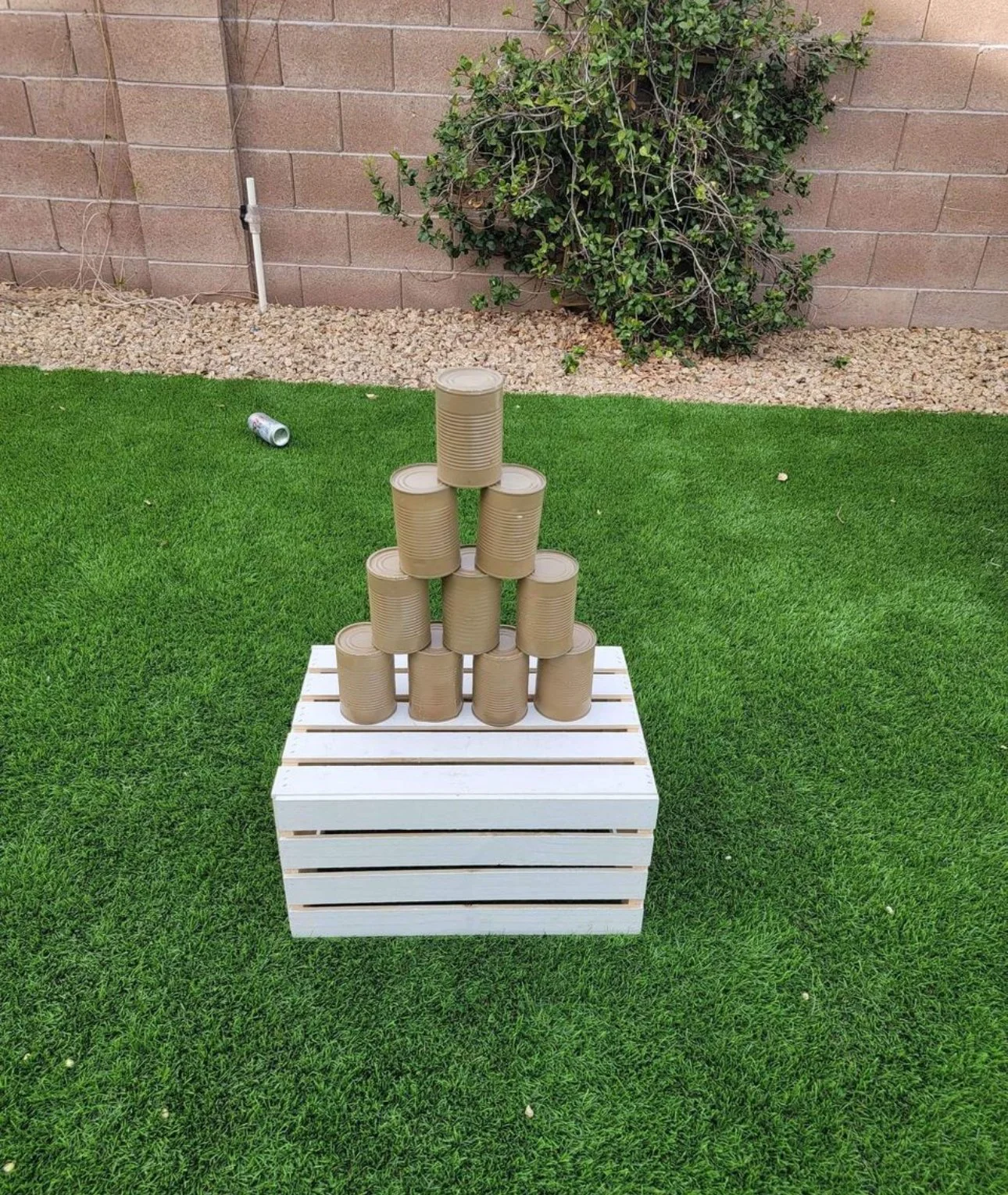 Pyramid of tin cans on a white wooden crate outdoors on grass
