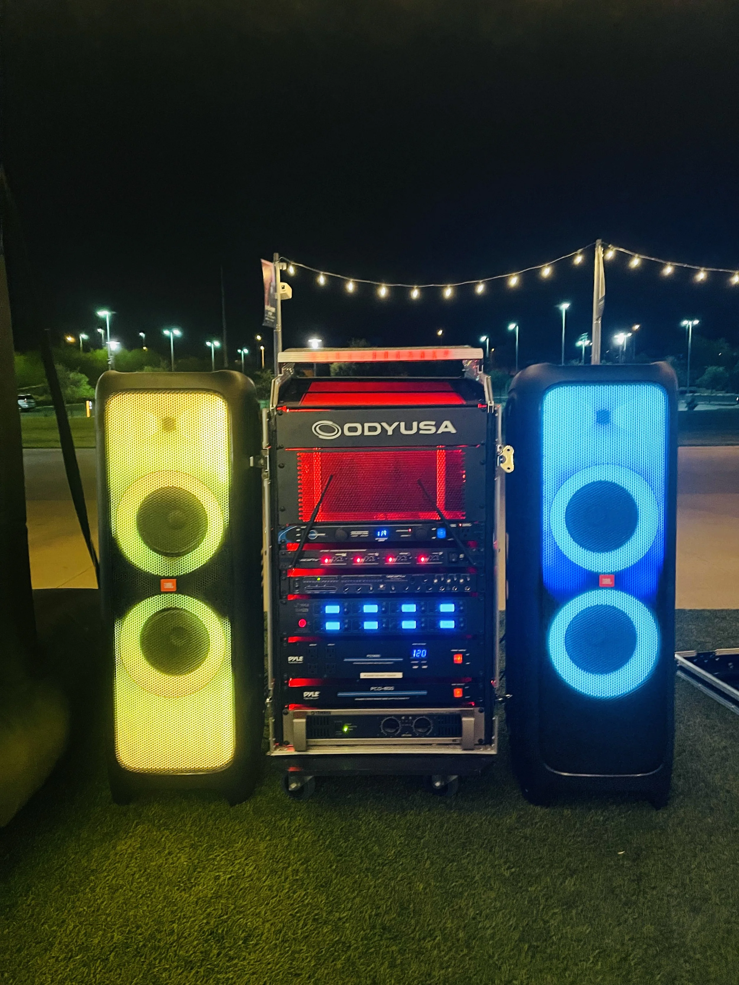 DJ equipment setup with illuminated speakers and sound system outdoors at night.