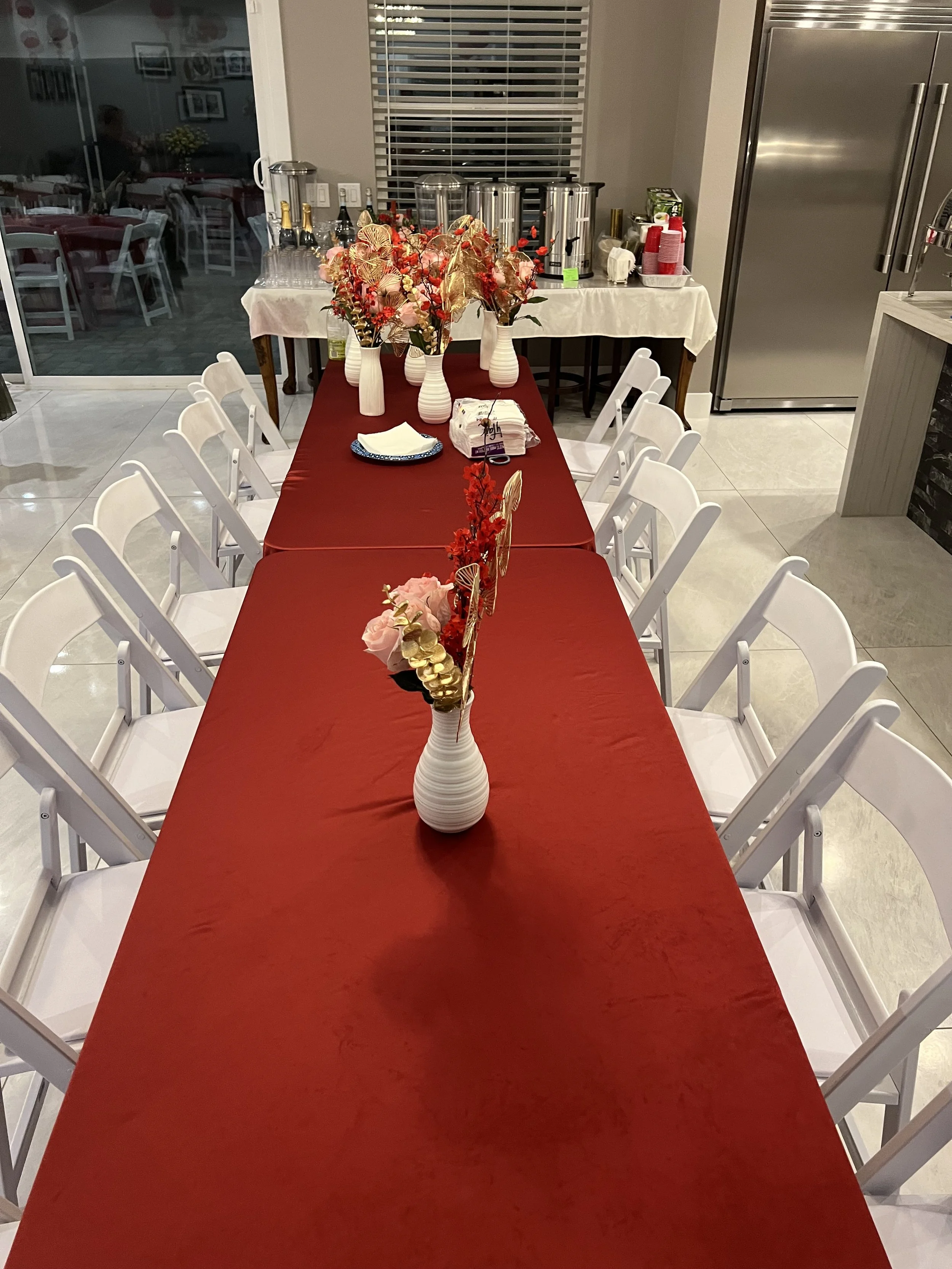 Elegant dining table setup with white chairs, red tablecloth, and floral centerpieces.