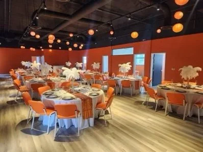 Elegant banquet hall with orange decor, tables, and feather centerpieces