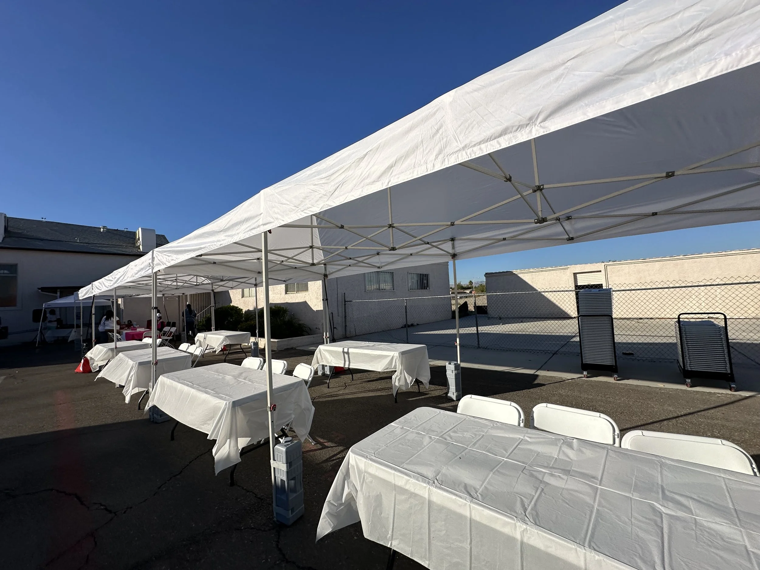 Outdoor event setup with white canopy tents, tables, and chairs