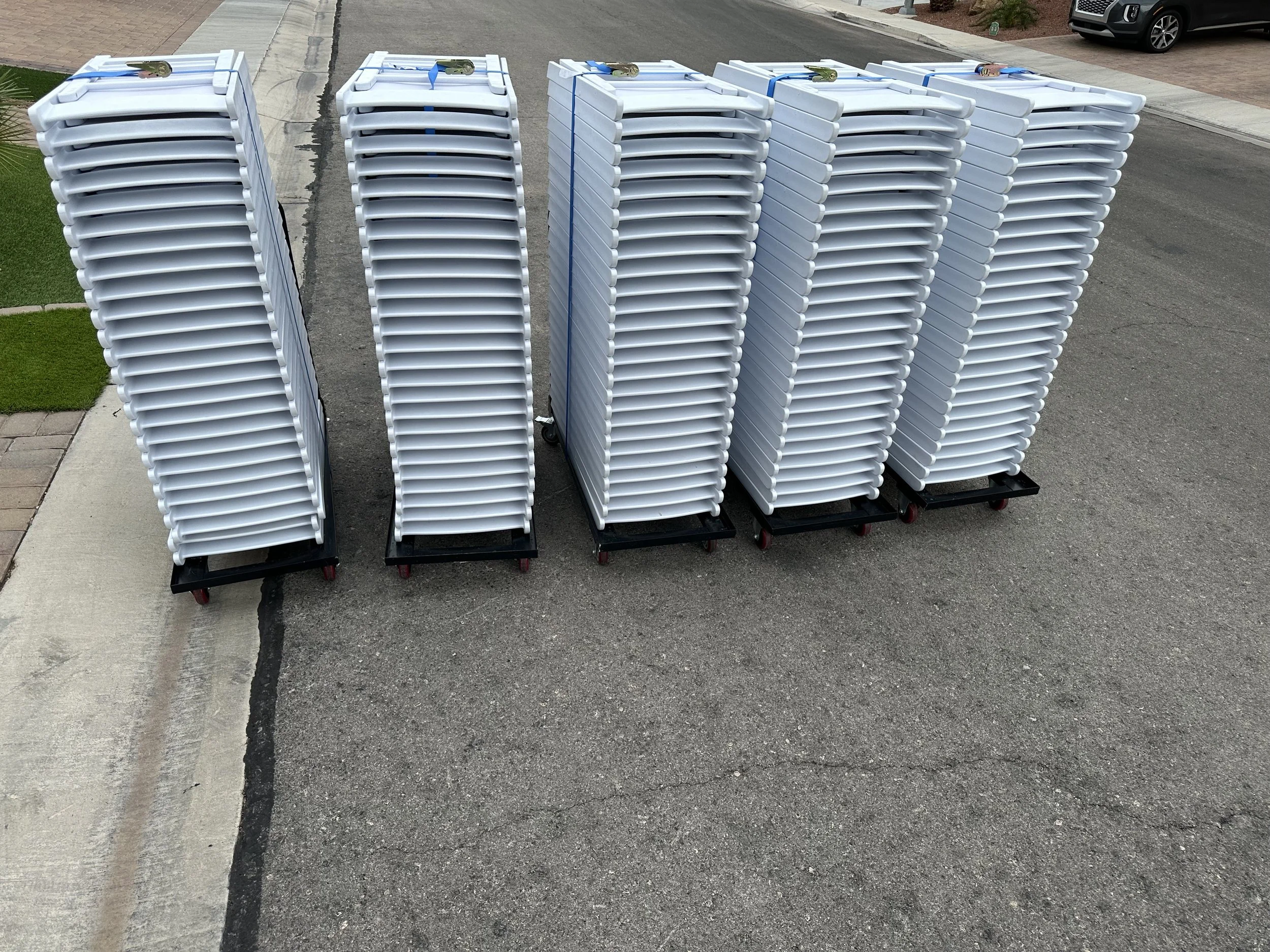 stacks of white plastic folding tables on carts on a street