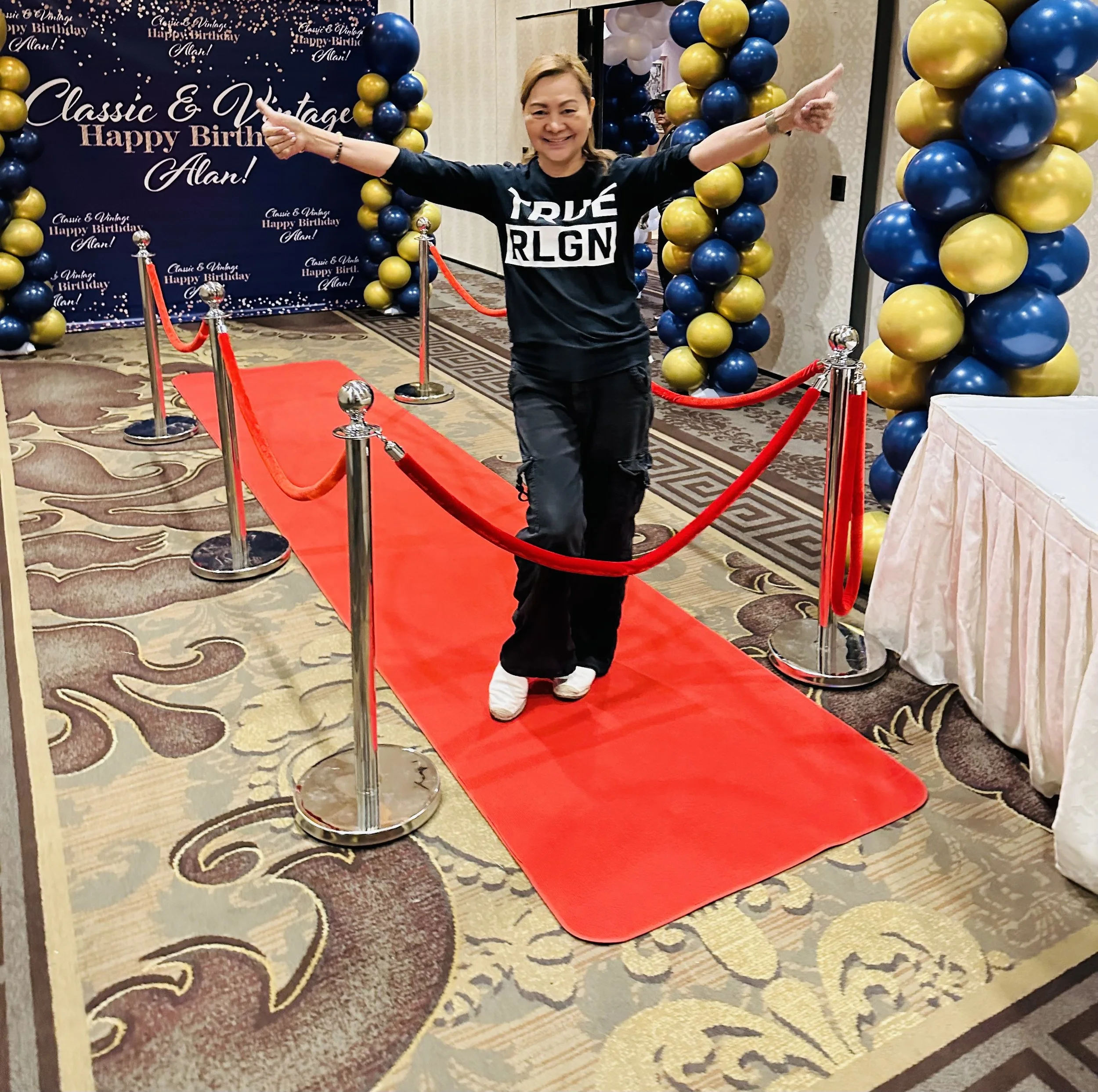 Person on a red carpet with balloons and birthday backdrop
