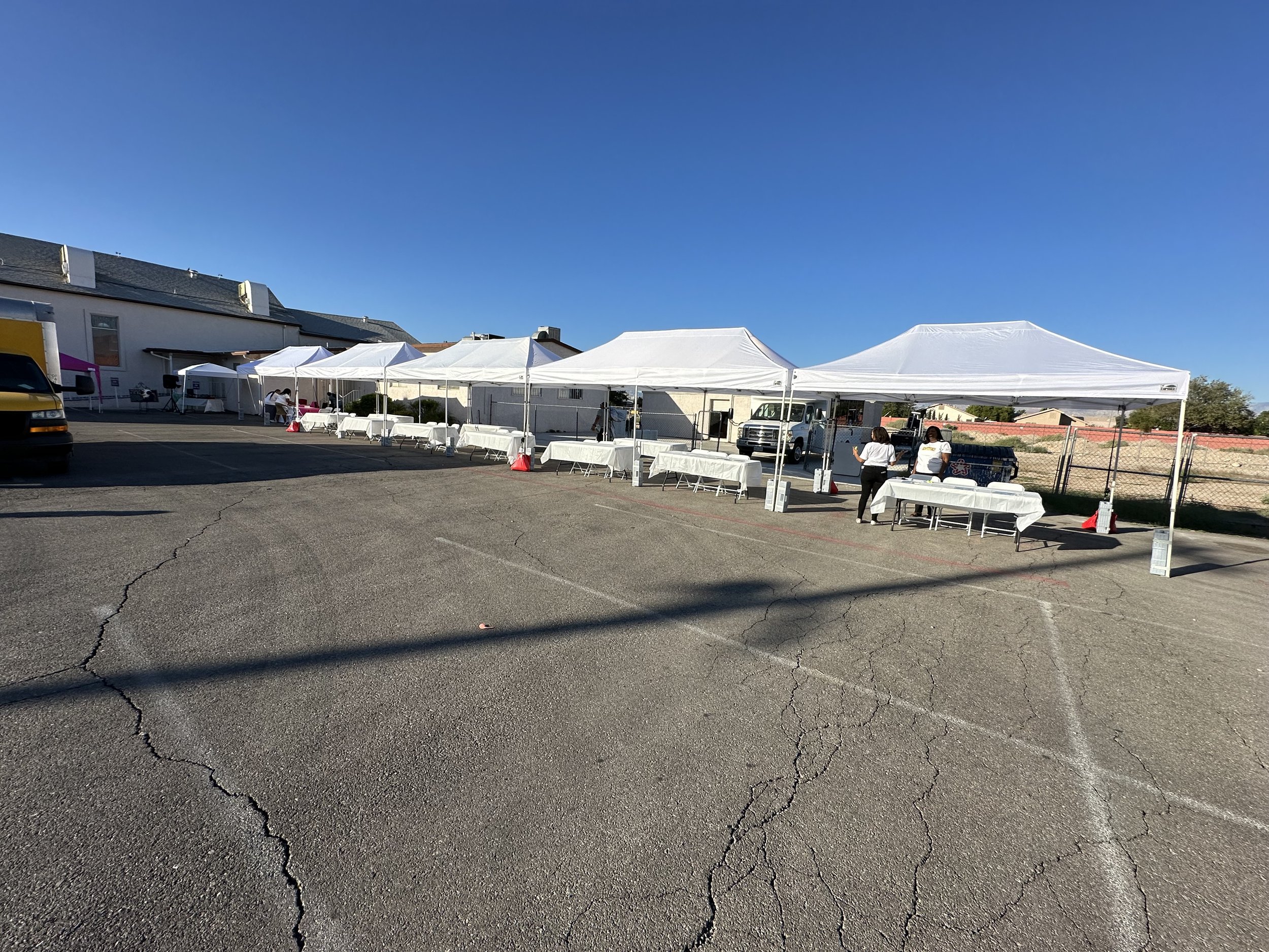Outdoor event setup with white tents and tables in a parking lot