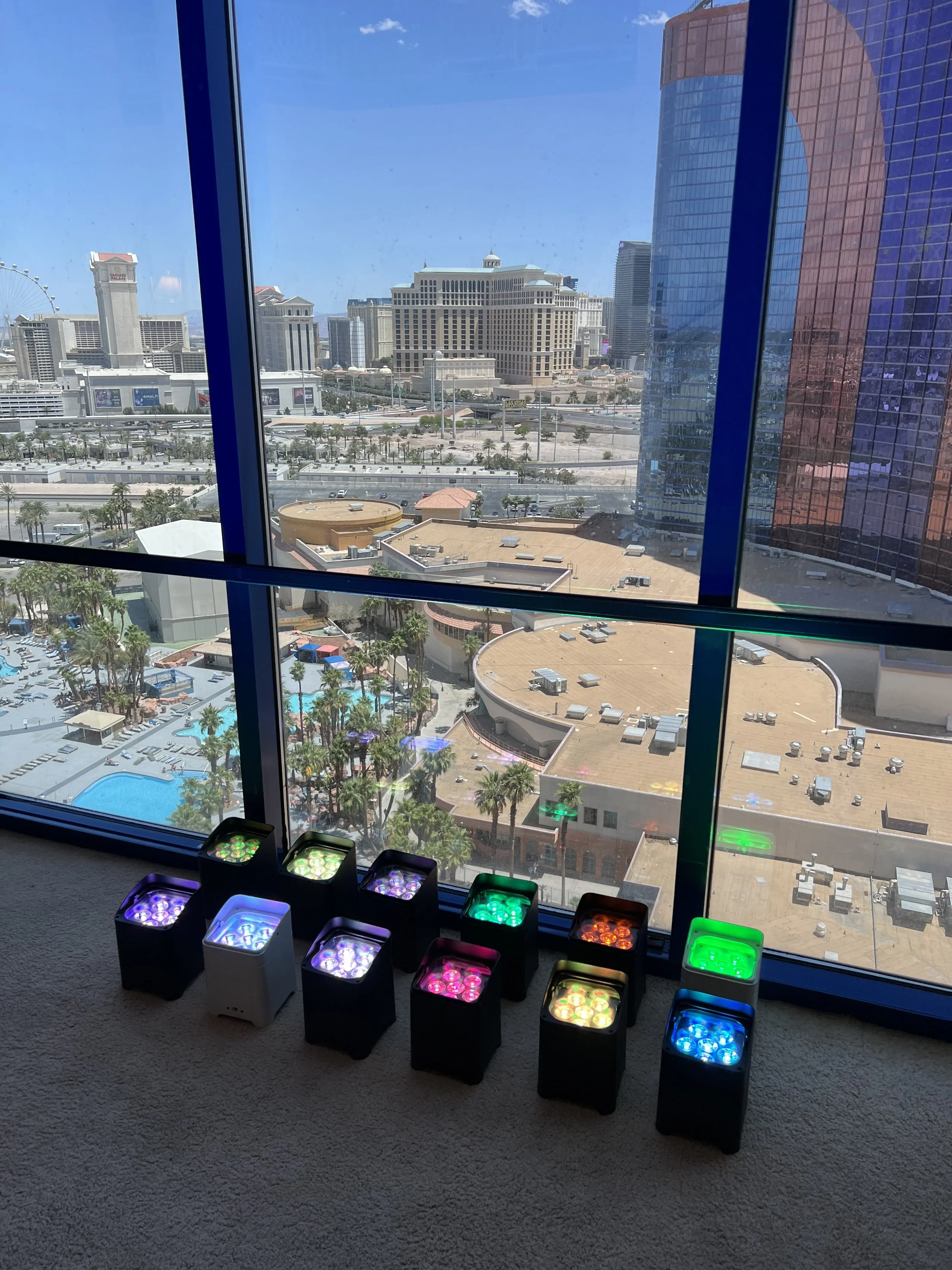Colorful LED lights inside a room with a view of a cityscape through glass windows, including high-rise buildings and a Ferris wheel.