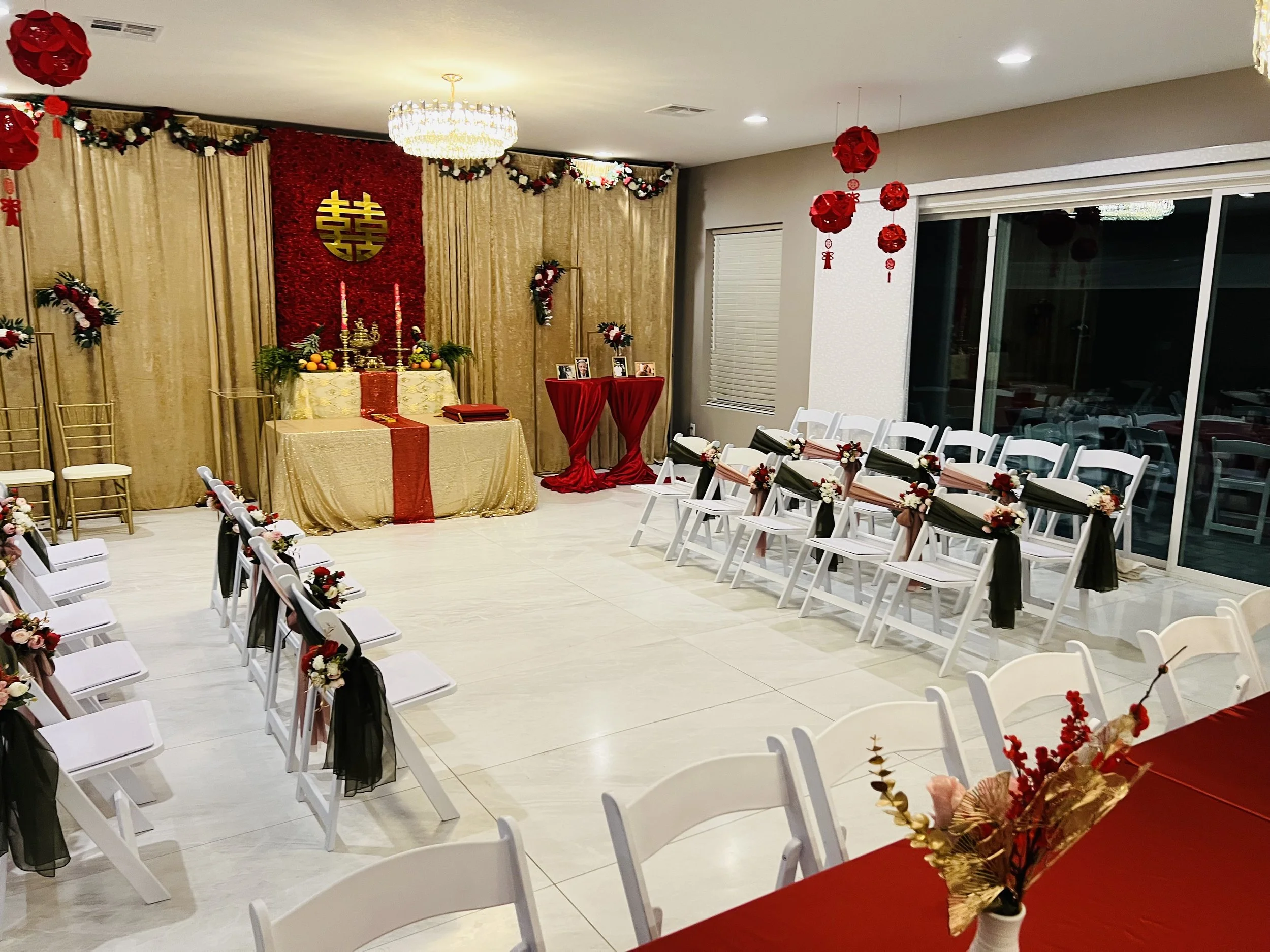 Indoor wedding ceremony setup with gold and red decorations, featuring a double happiness symbol, arranged chairs, and a floral altar.