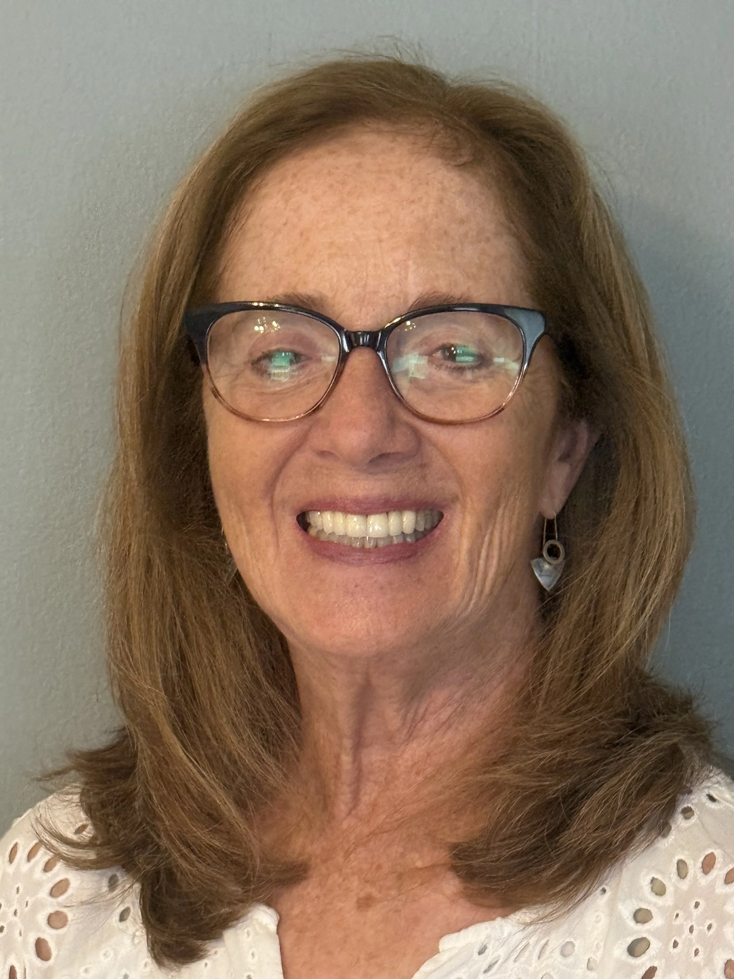 Woman with blonde hair and glasses smiling in front of a gray background