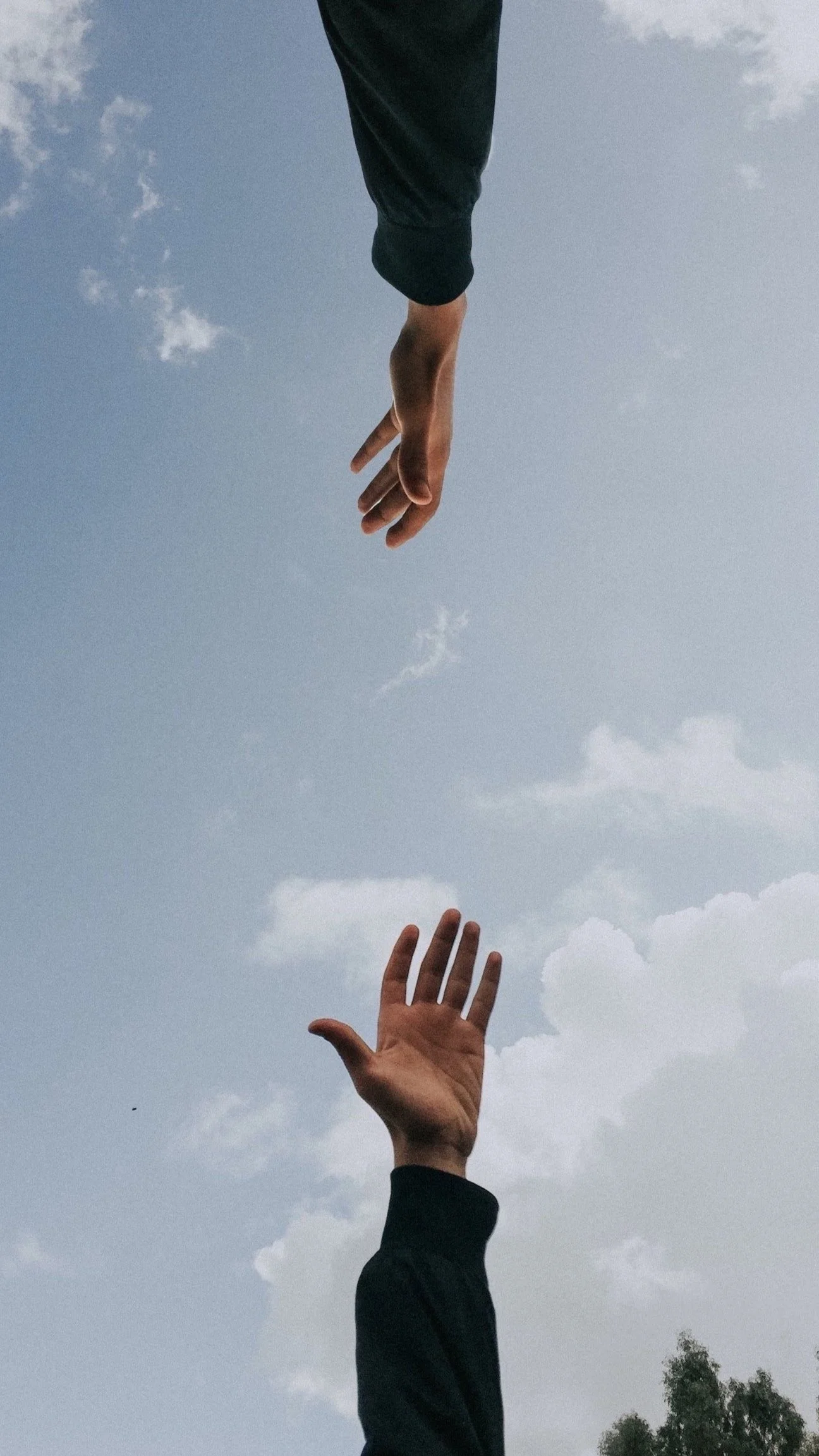 Two hands reaching towards each other against a cloudy sky background.