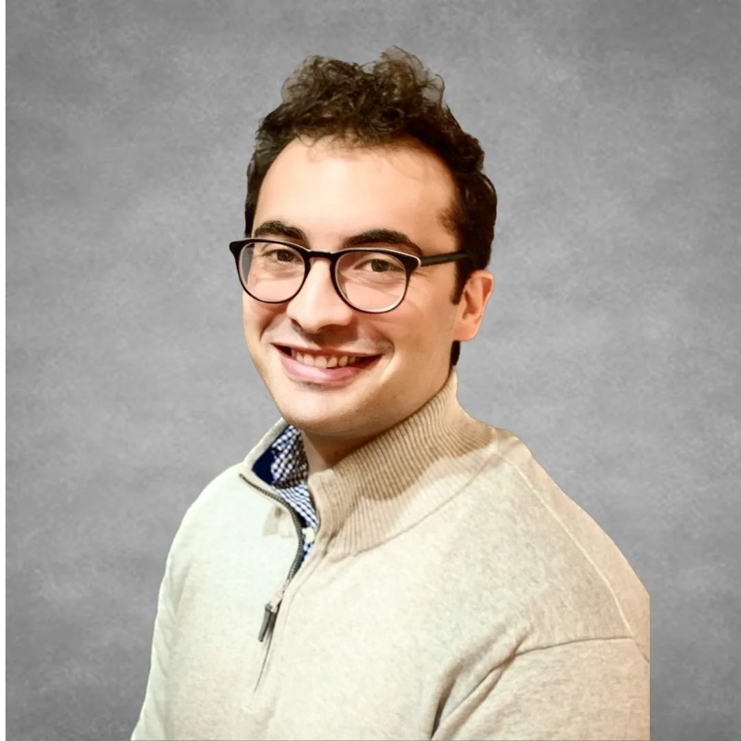 Smiling person with glasses wearing a beige zip-neck sweater against a gray background.