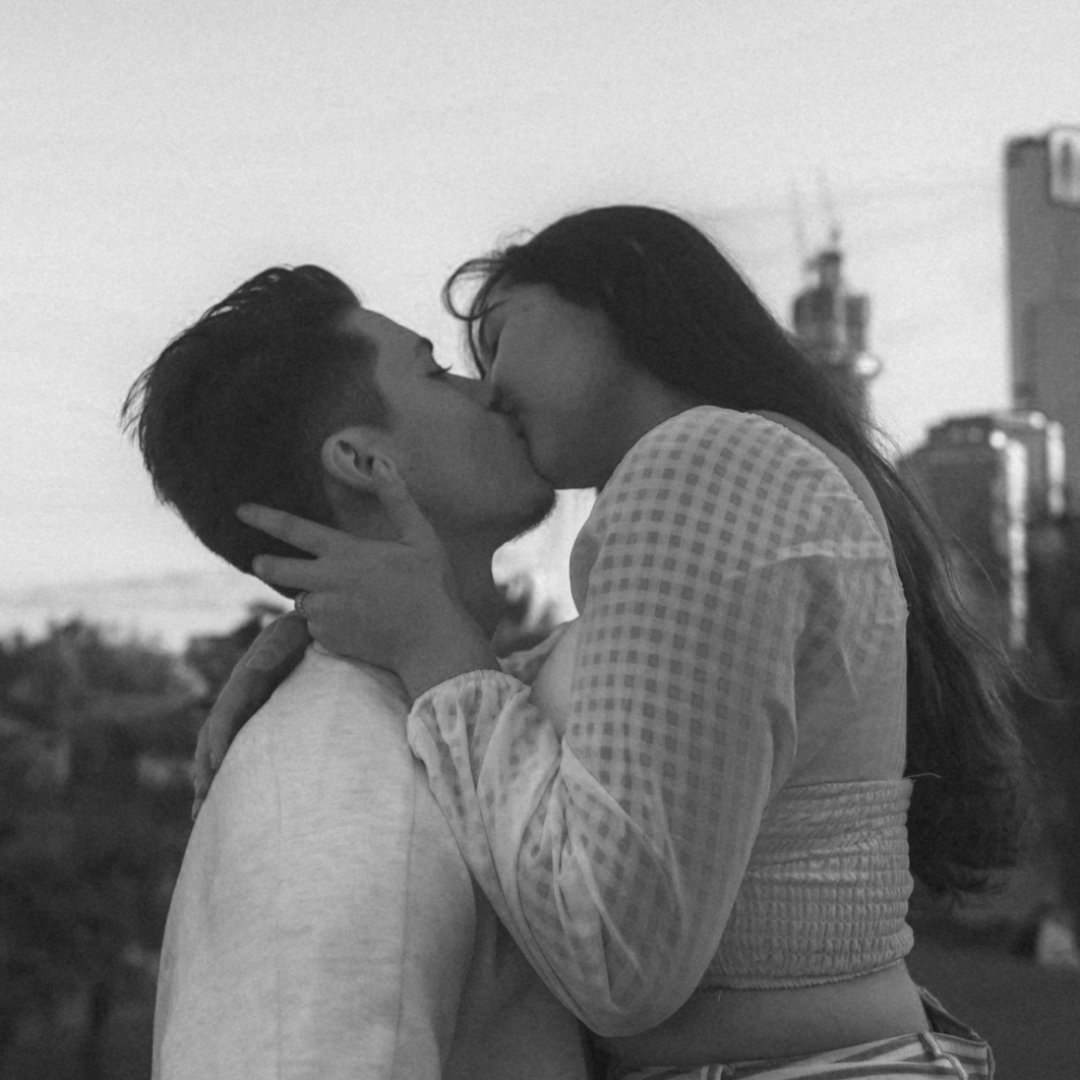 A black and white photo of a man and woman kissing outdoors, with the woman holding the man's face gently.