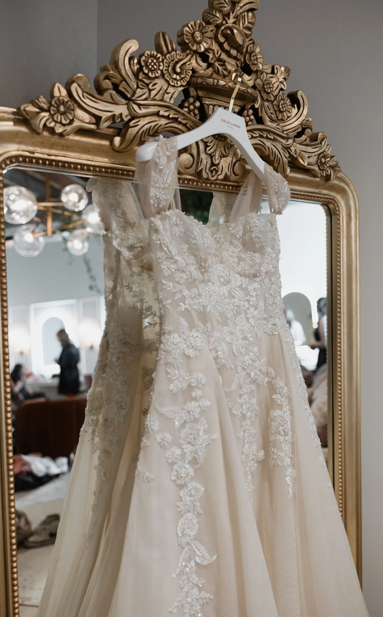 Elegant wedding dress with lace and floral embroidery hanging on a decorative mirror.