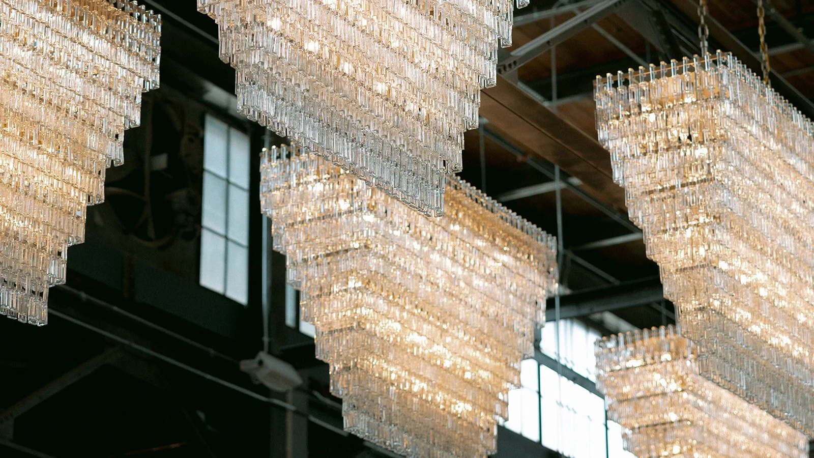 Multiple large crystal chandeliers hanging from a high ceiling, illuminated and reflecting light.