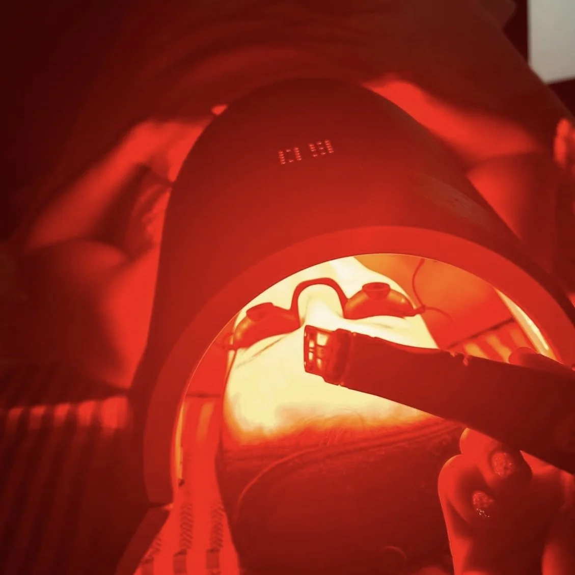 A person's leg under a red light, with a device around their ankle connected to wires, possibly during a medical or therapeutic procedure.