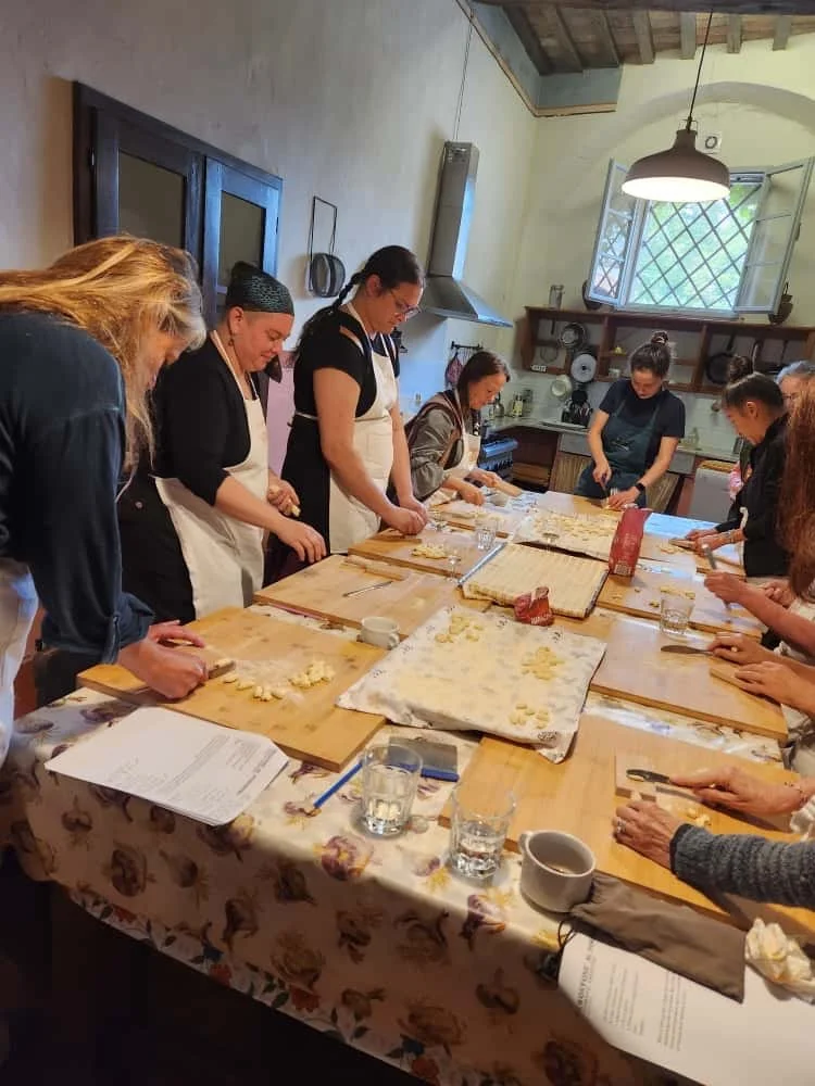Group of women standing around a kitchen table, preparing dough for cooking or baking.