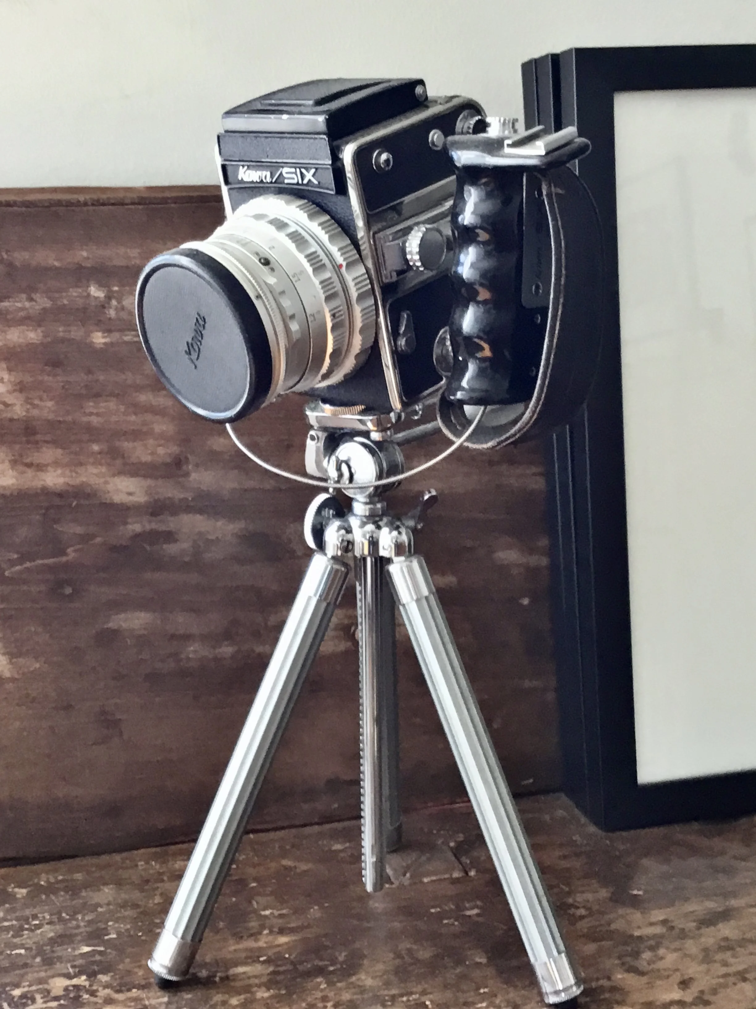 A vintage film camera on a tripod, positioned on a wooden surface.