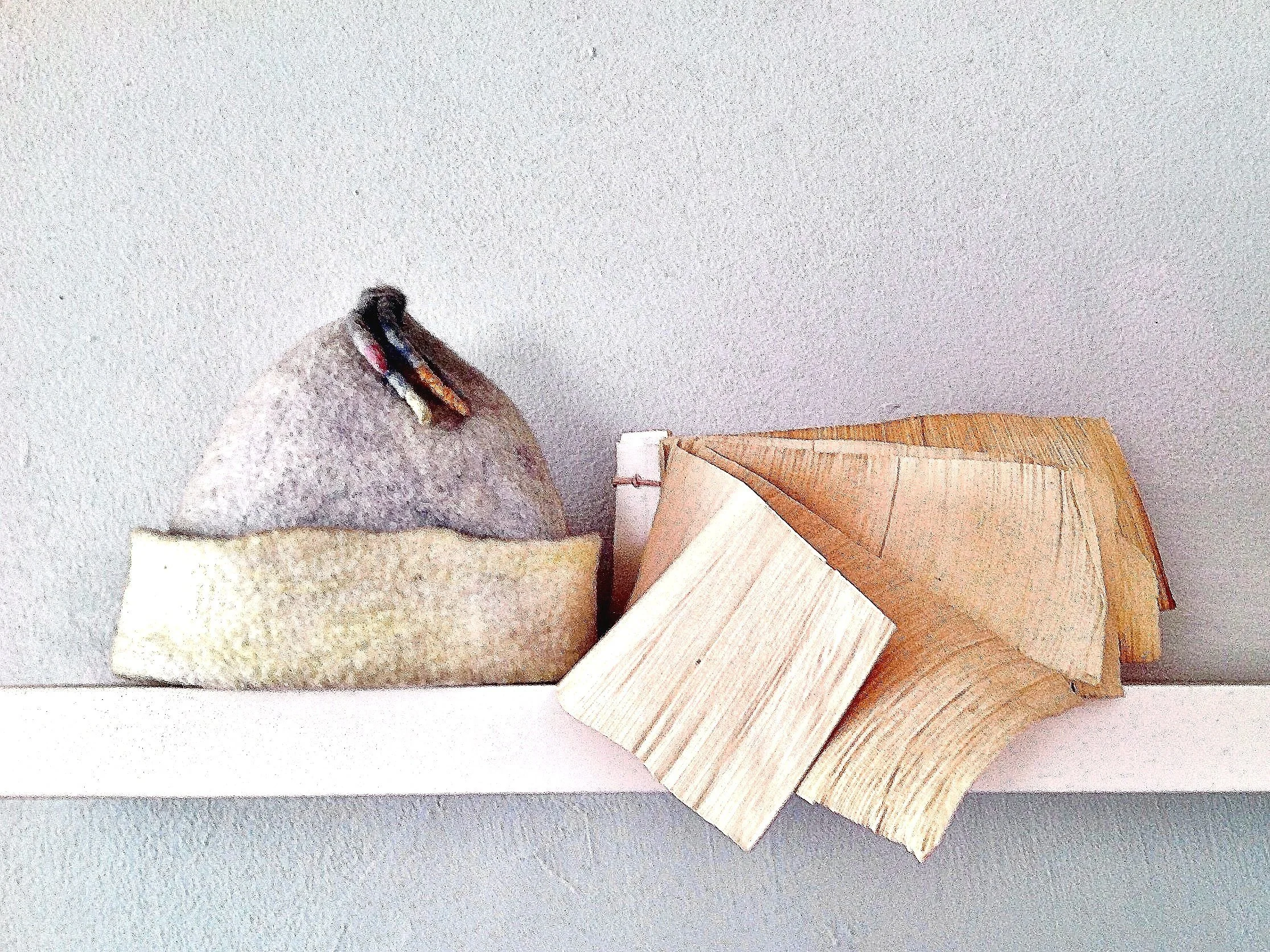 A decorative display with a felted bird figure on the left, surrounded by wooden pieces on the right, set against a plain wall background.